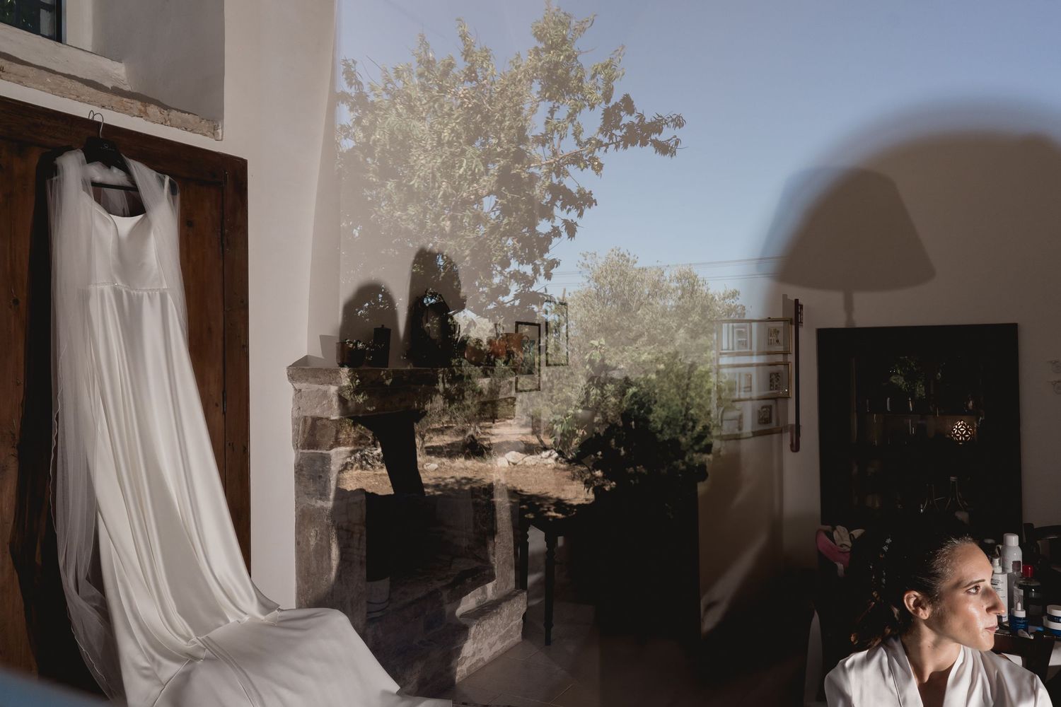 Wedding dress hanging in doorway with natural light streaming through window.
