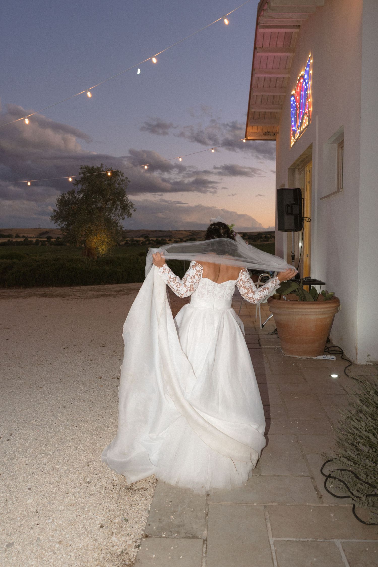 White wedding dresses illuminated by string lights against a sunset backdrop at an outdoor venue.