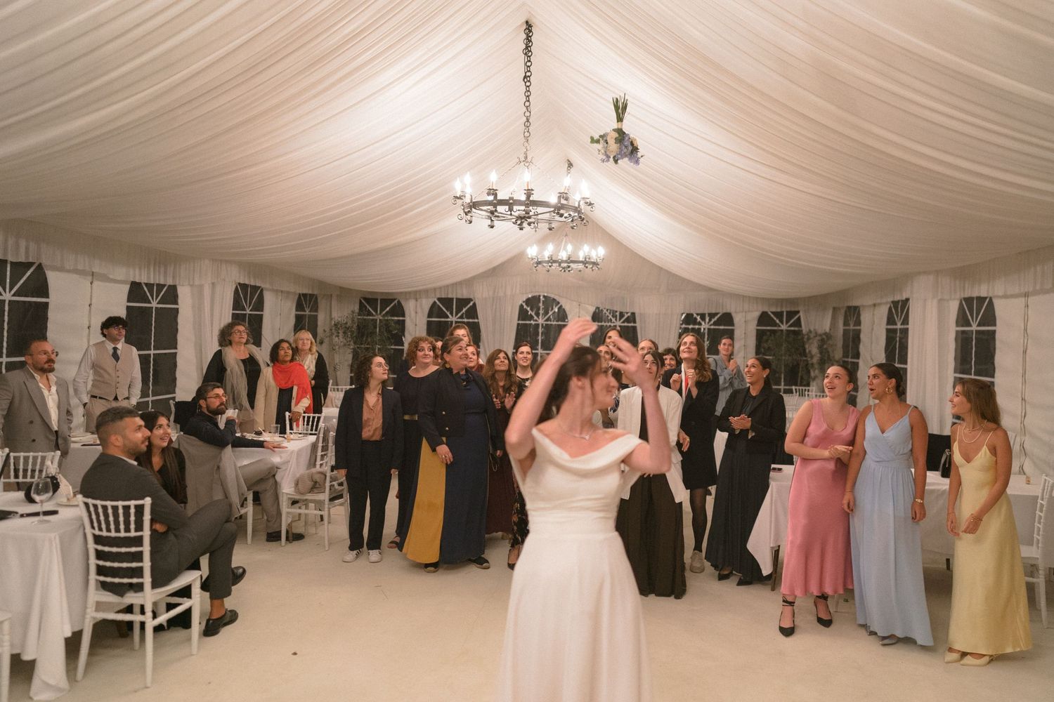 Wedding reception in an elegant white tent with chandelier lighting and guests dancing.