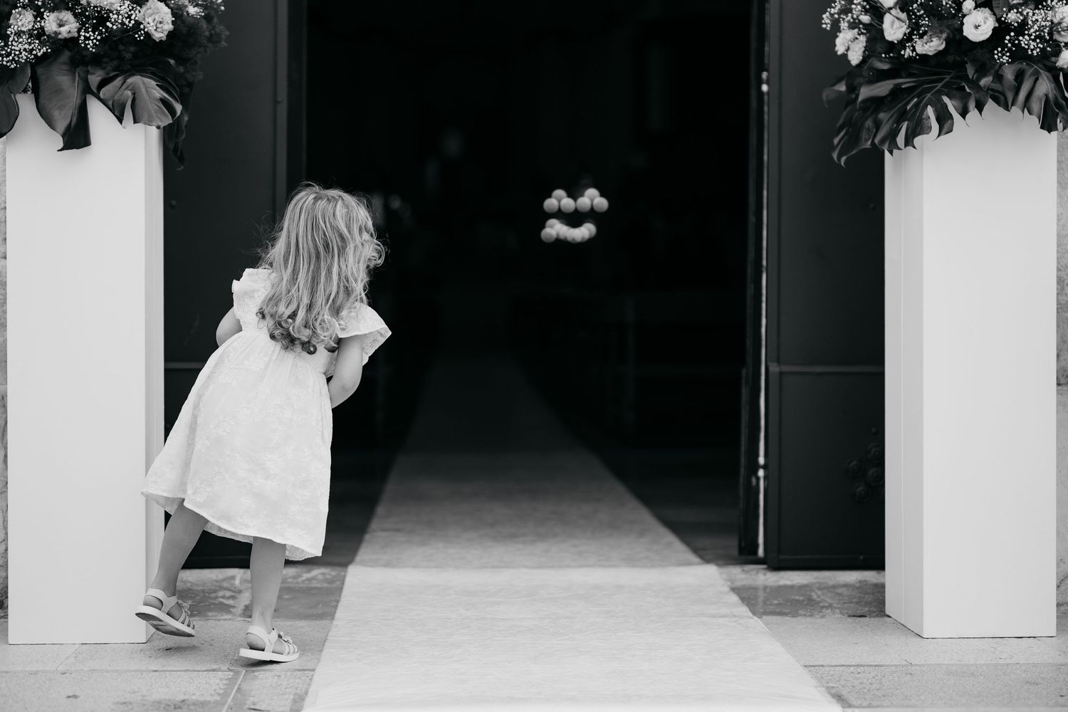 Outdoor church entrance with white floral decorations and guests arriving for a wedding.