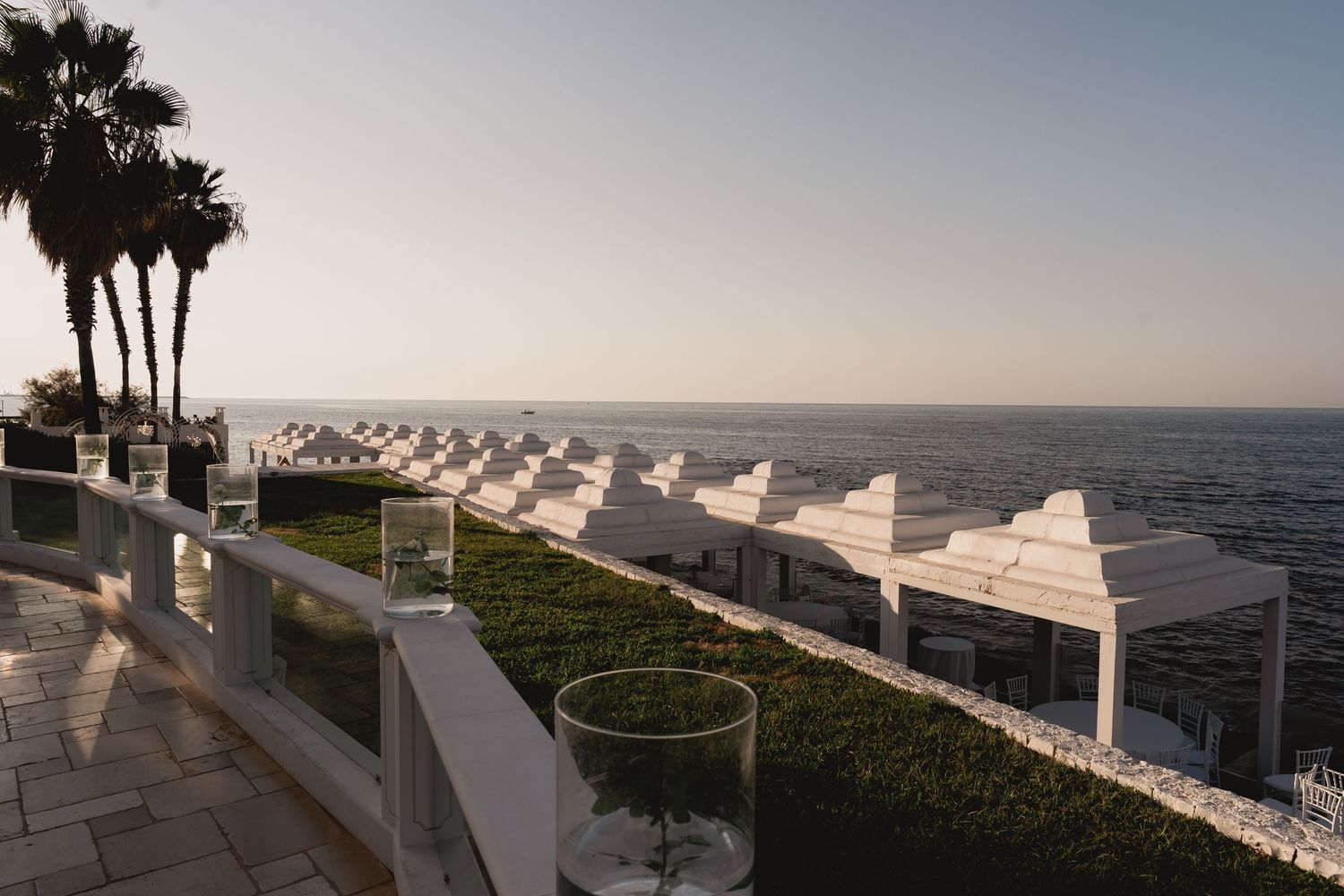 Oceanfront wedding venue with white pergolas and palm trees at sunset.