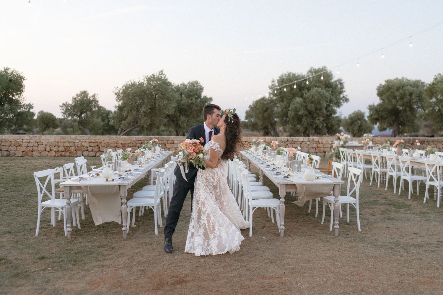 Outdoor wedding reception setup with white chairs and tables arranged on grass.