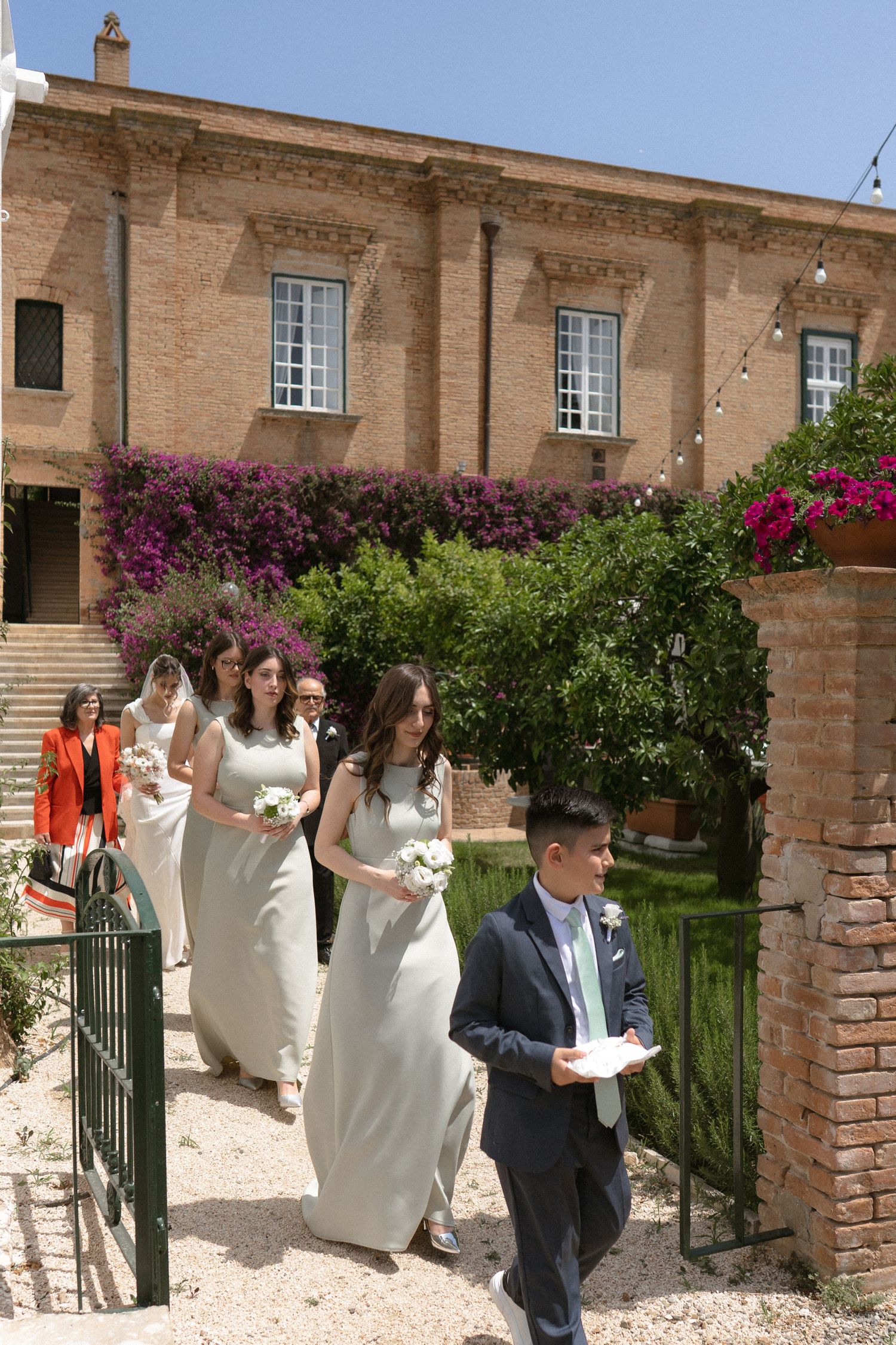 Wedding party walking along a garden path with blooming bougainvillea and stone architecture.