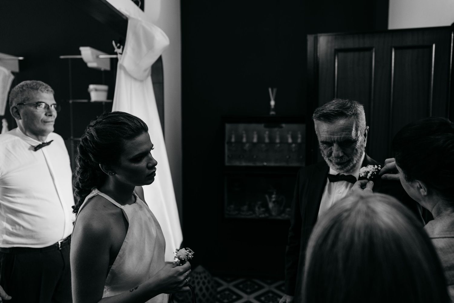 A candid black and white photograph showing people in formal attire having a conversation indoors.