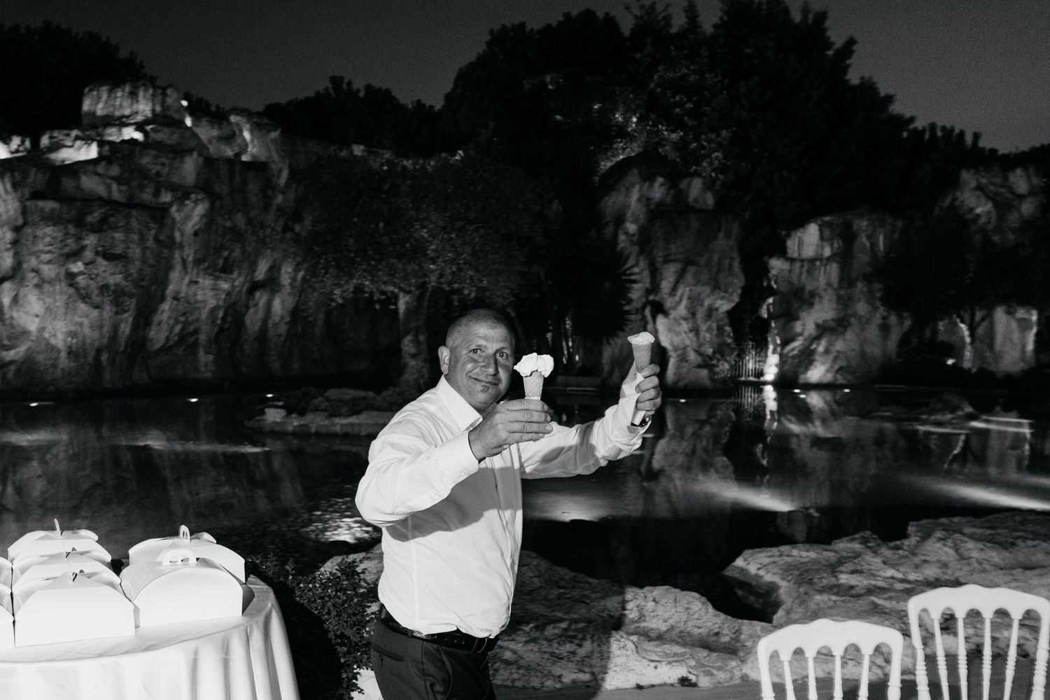 Person joyfully dancing outdoors at night with stone cliffs and party tables in the background.