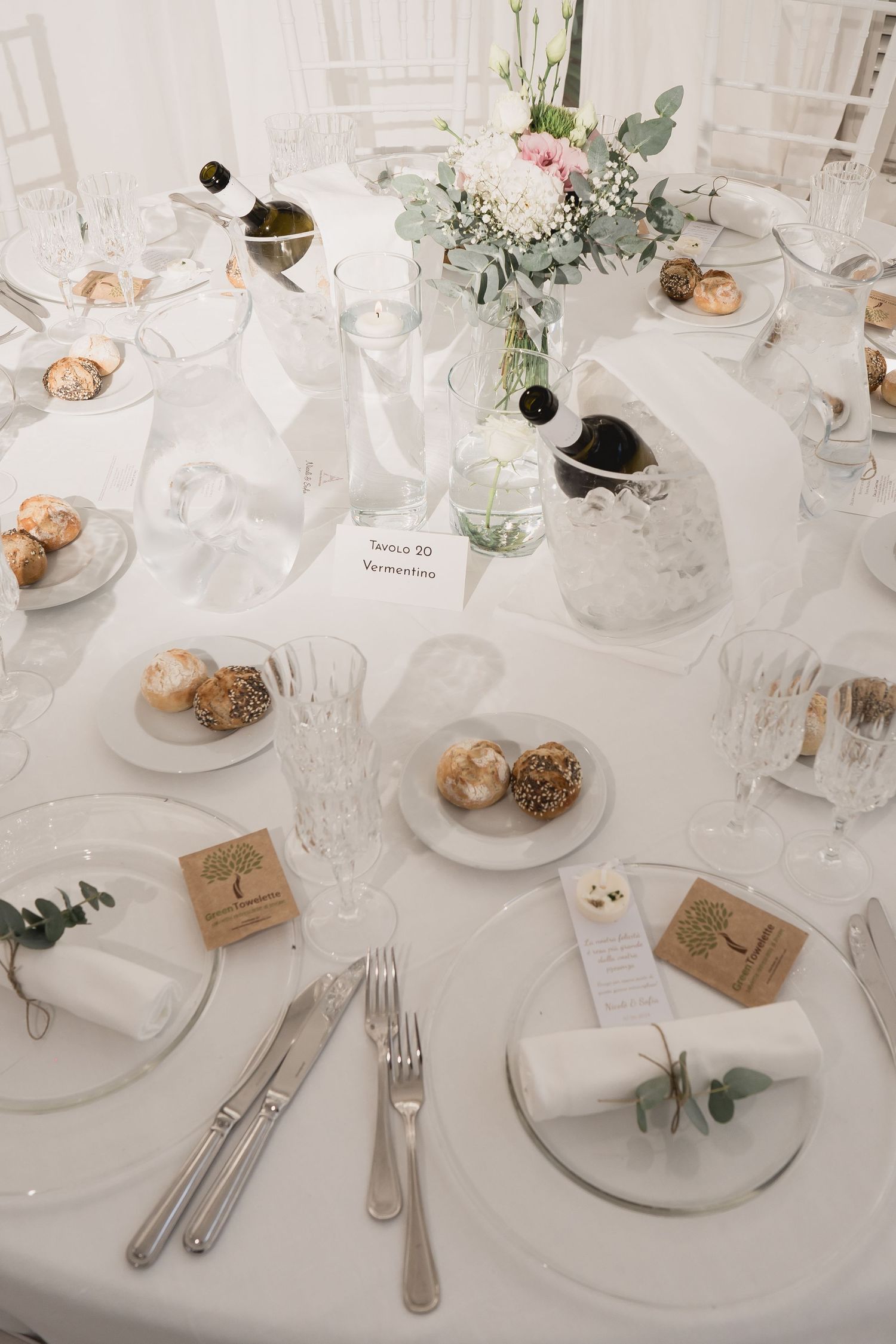 Elegant white wedding table setting with floral centerpieces, place cards, and delicate tableware.