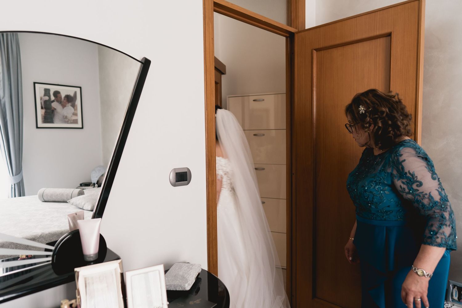 A glimpse of wedding preparations through a doorway with a white dress visible.