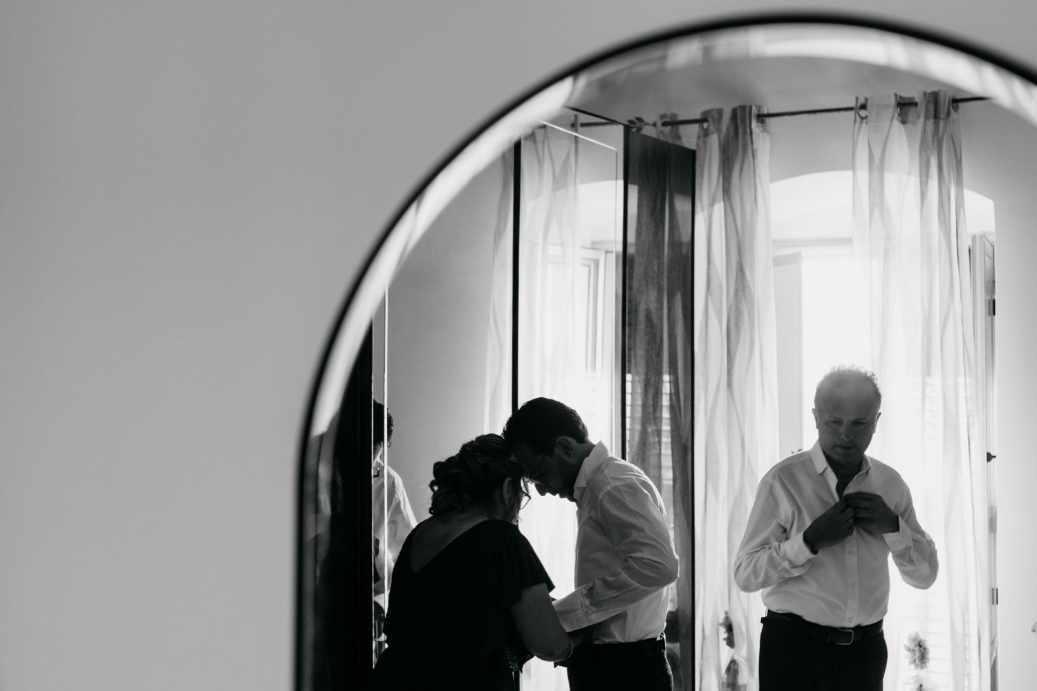 Black and white reflection of wedding preparations through arched doorway.