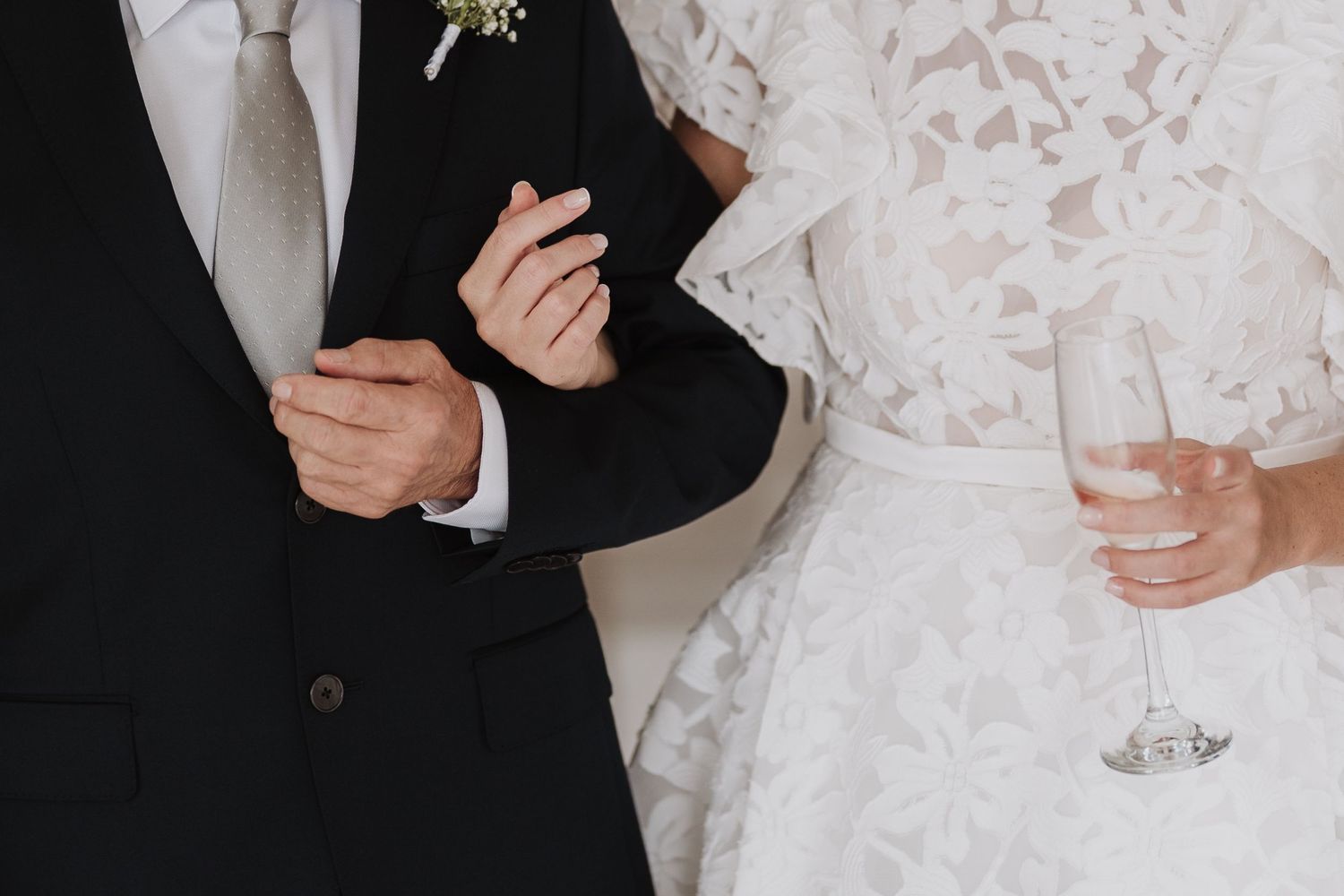 Close-up of formal wedding attire showing a black suit, white tie, and lace dress details.