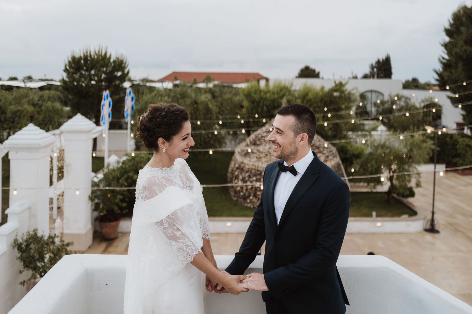 A couple sharing an intimate moment on a rooftop terrace with string lights and white decor.