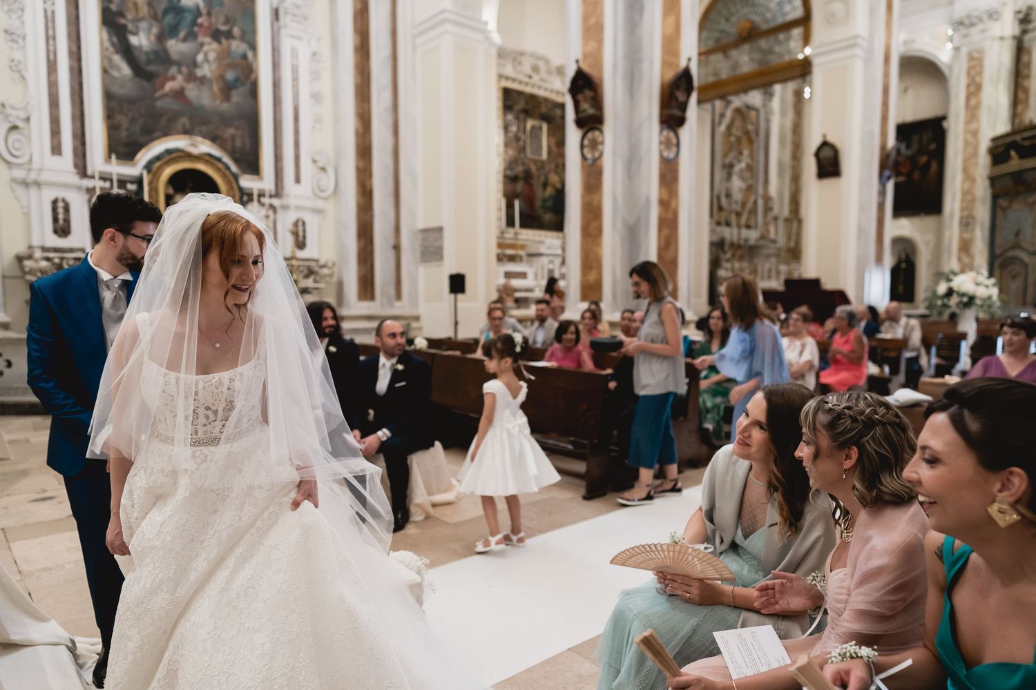 A wedding ceremony takes place inside an ornate Catholic church with guests watching from wooden pews.