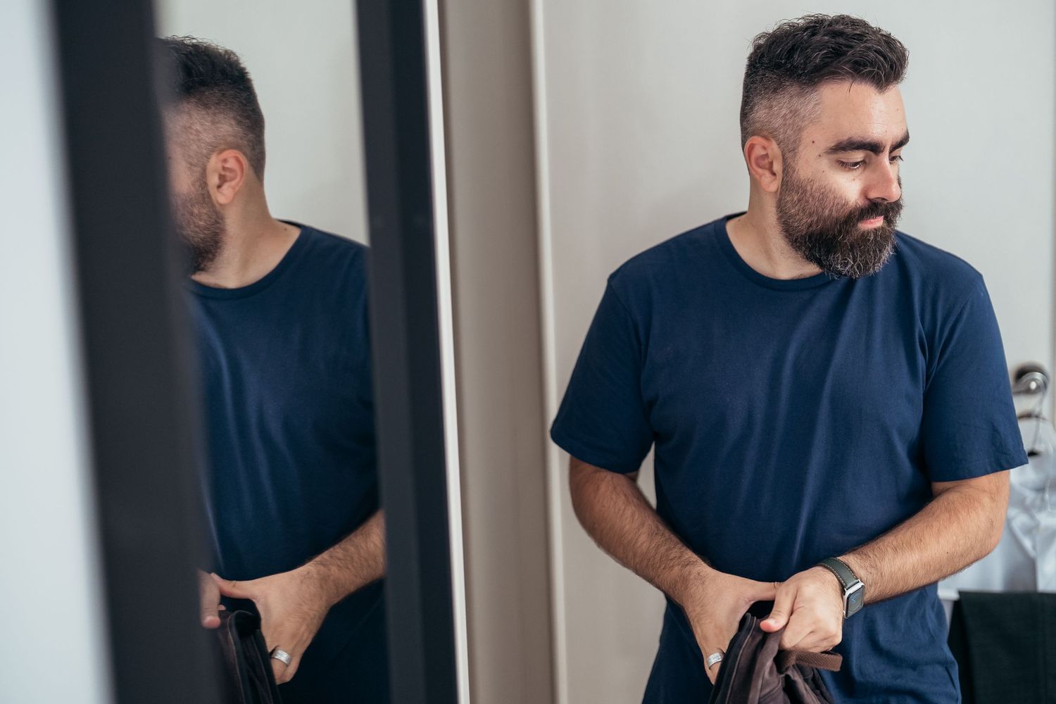 A reflection in a mirror shows a person adjusting their navy blue t-shirt.