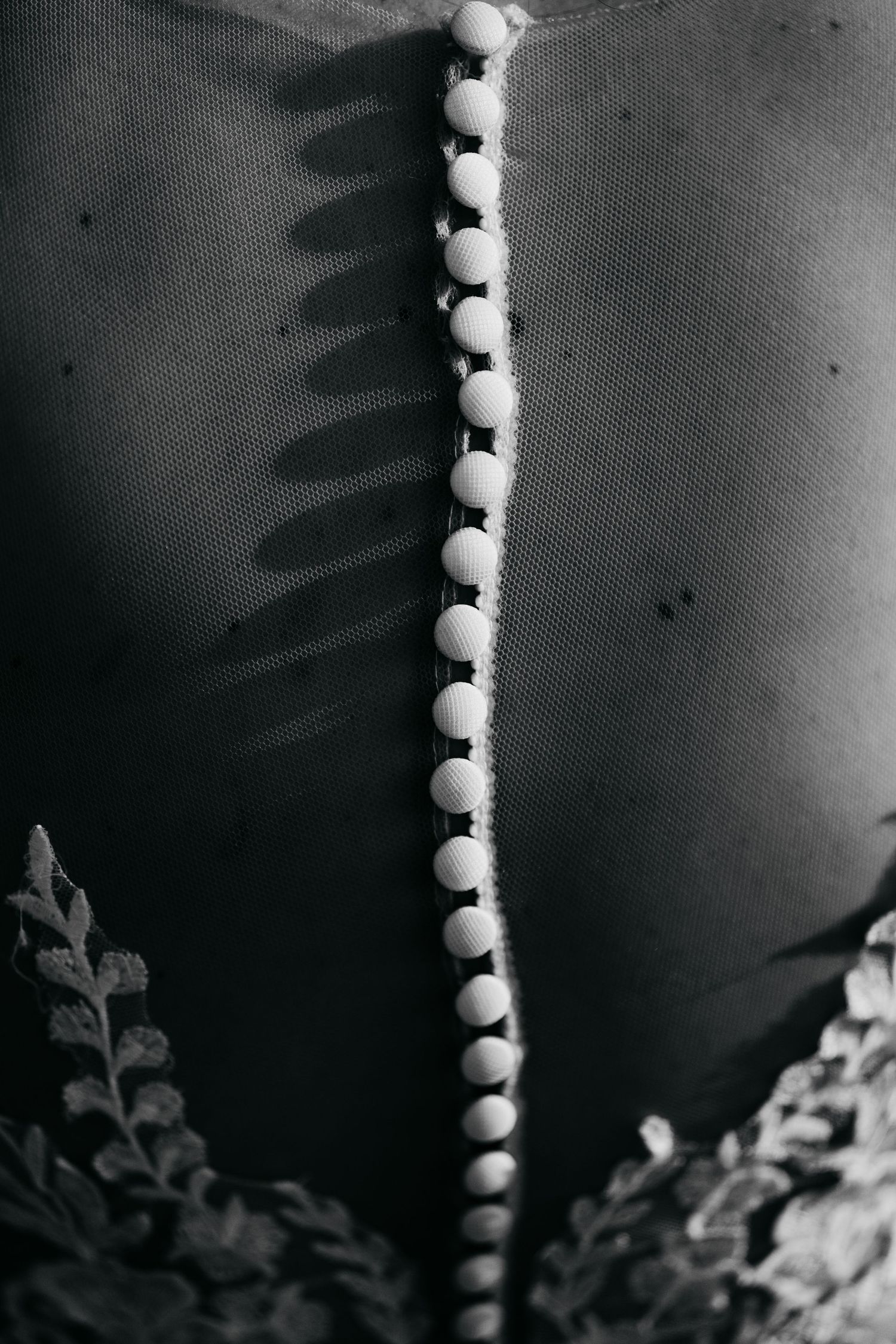 Close-up black and white detail of pearl button closure down back of bridal lace wedding gown.