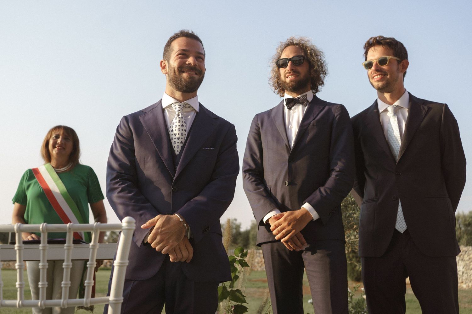 Wedding party stands outdoors in formal attire with mountain views in the background.