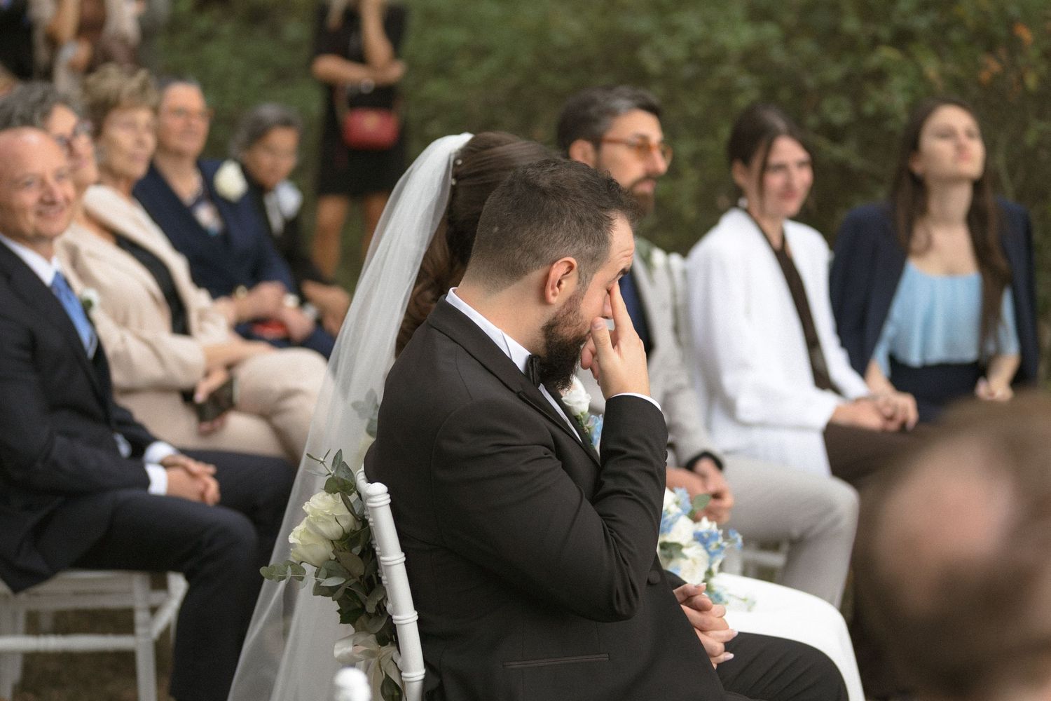 Wedding guests seated outdoors for a ceremony among trees and natural surroundings.