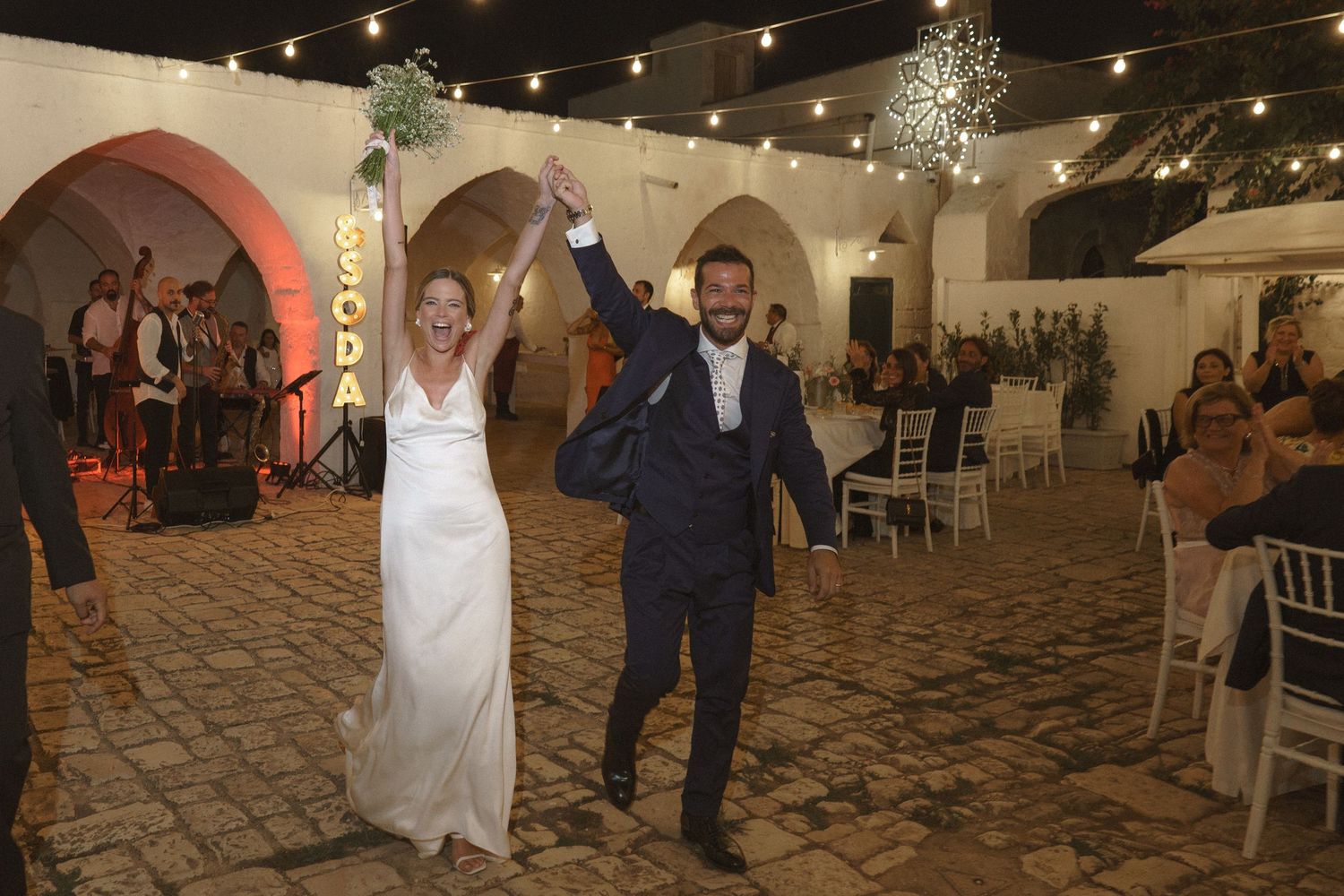 Joyful newlyweds dance together under string lights at their reception venue.