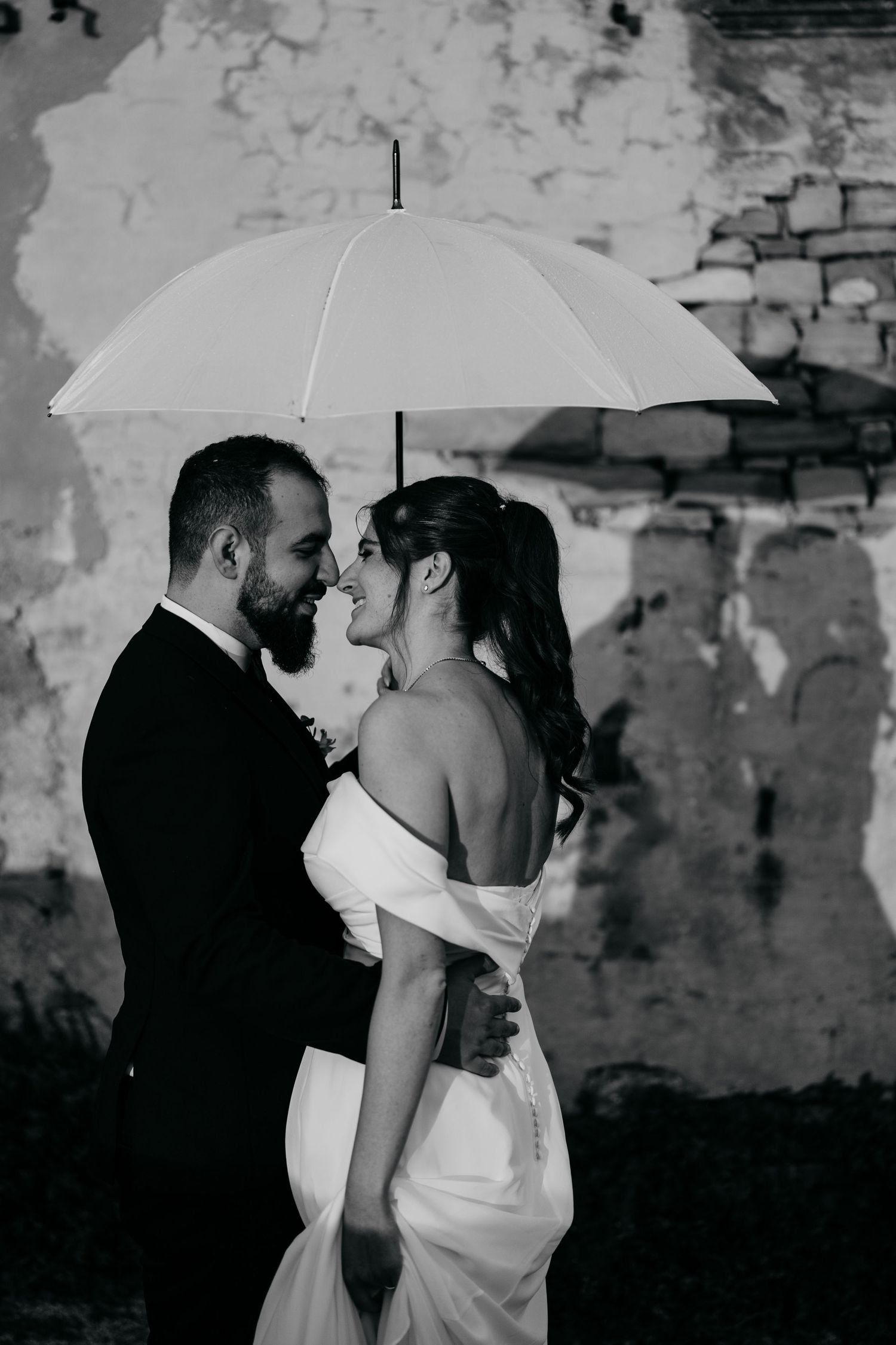 Romantic black and white photo of a couple sharing an intimate moment under white umbrellas.
