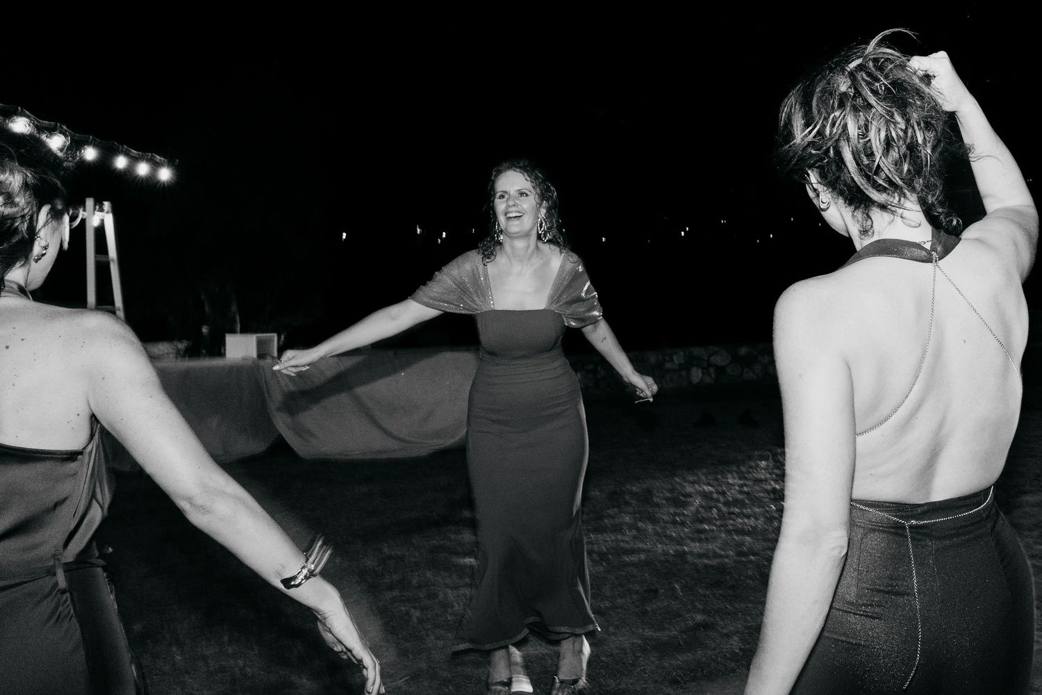 Three people dancing together outdoors at night in vintage 1950s style clothing and skirts.