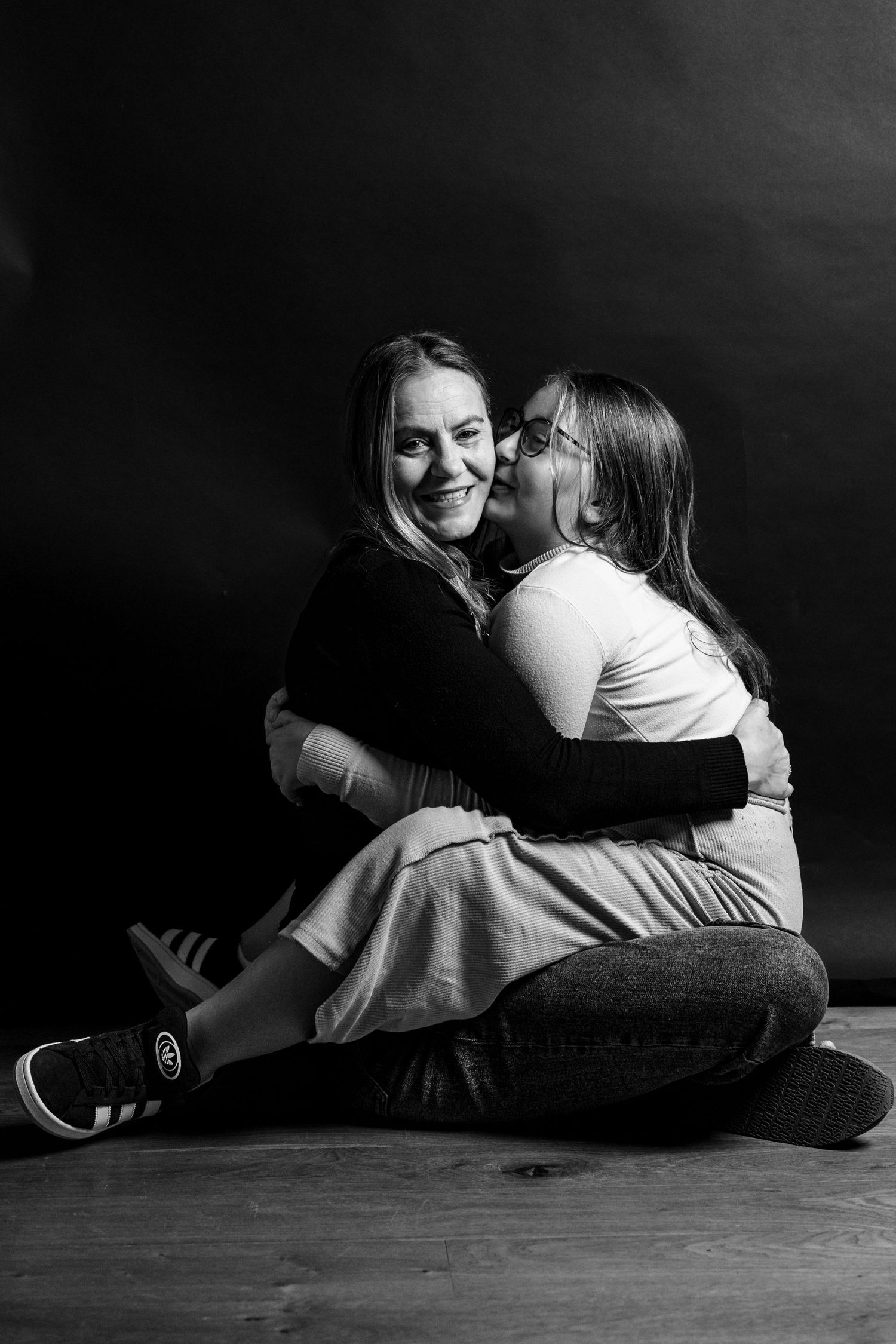 A heartwarming black and white studio portrait showing two people embracing and laughing together on the floor.