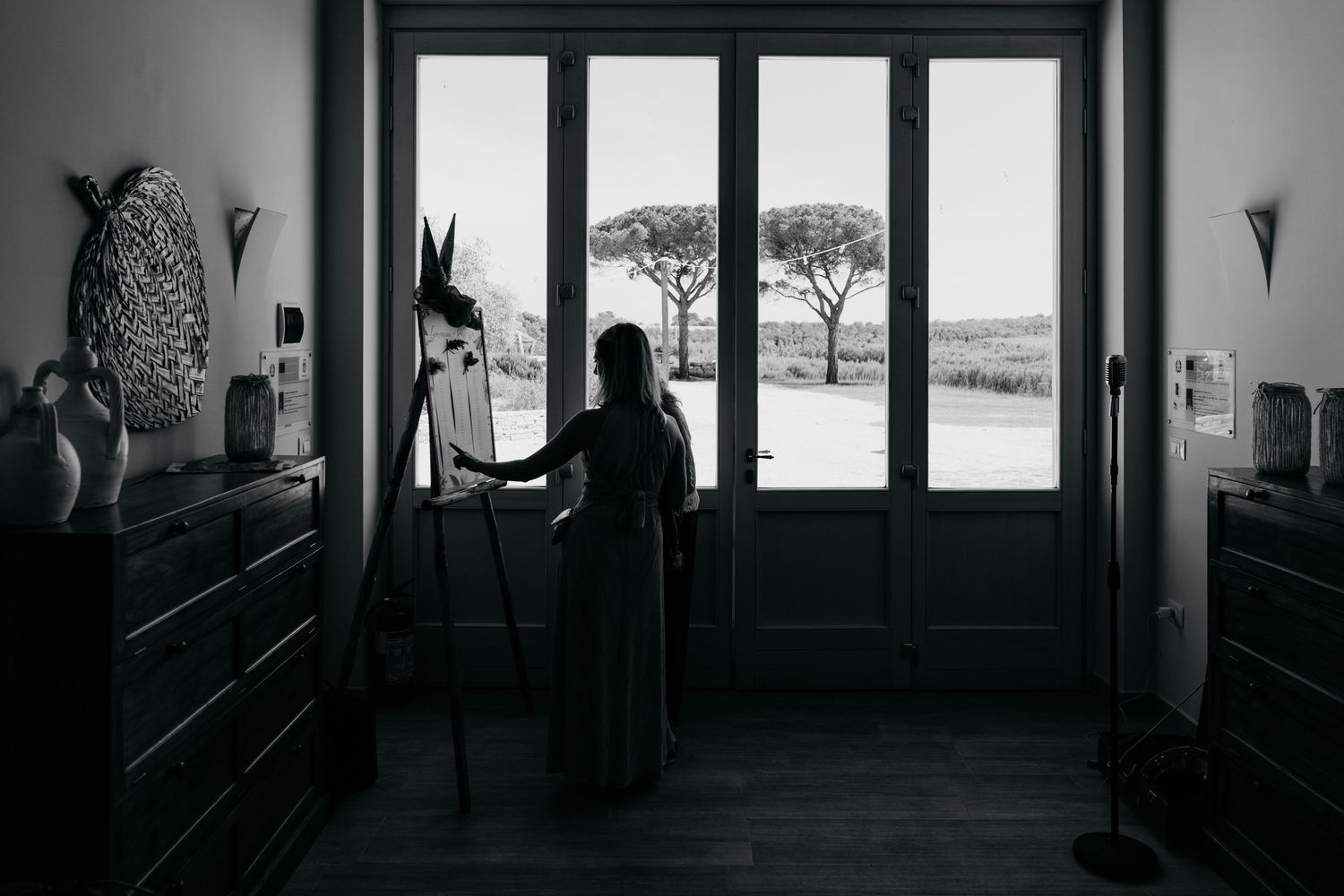 Silhouetted figures stand in a dark hallway with large windows overlooking a scenic landscape.