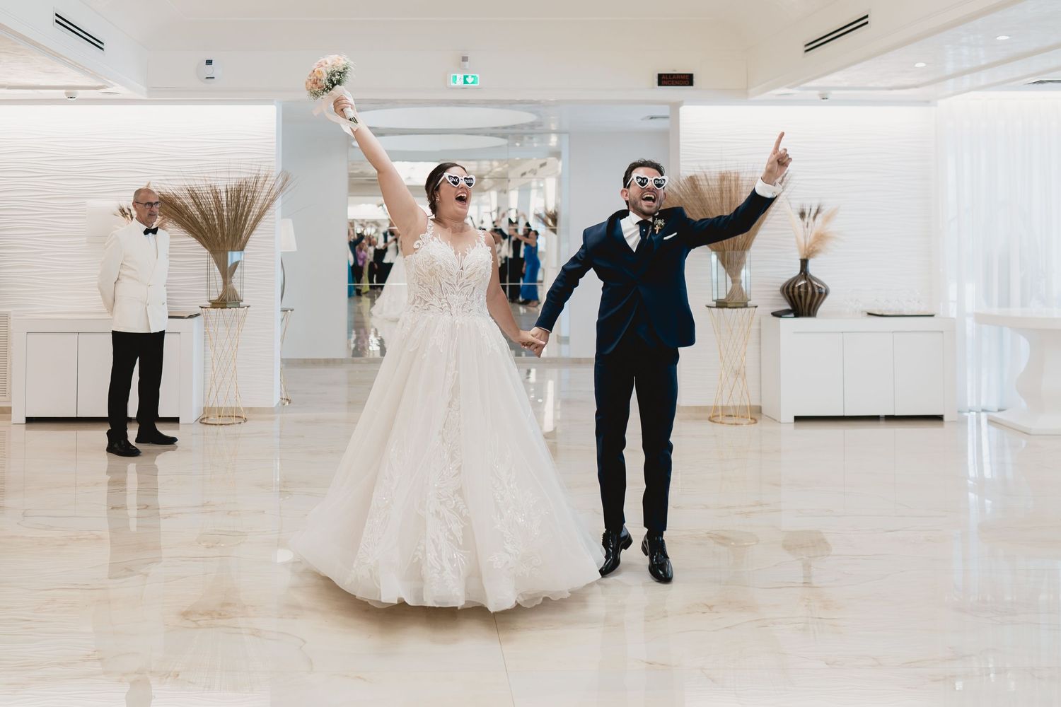 Newlyweds celebrating with raised arms in a bright modern reception venue.