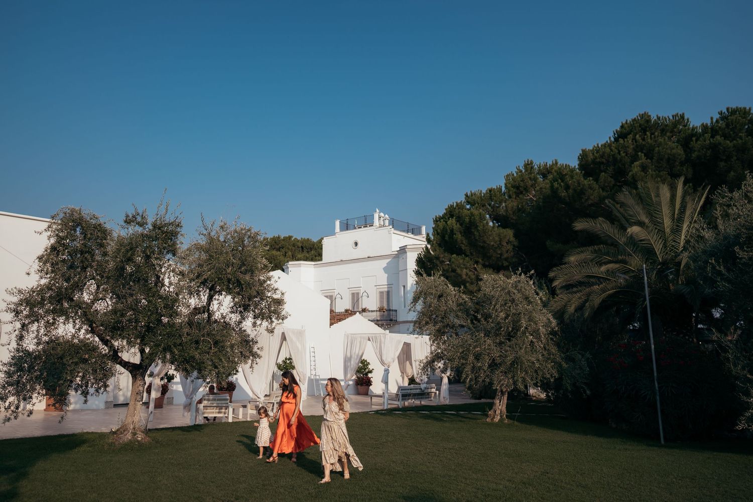 Mediterranean style white building surrounded by palm trees and greenery during a wedding celebration.