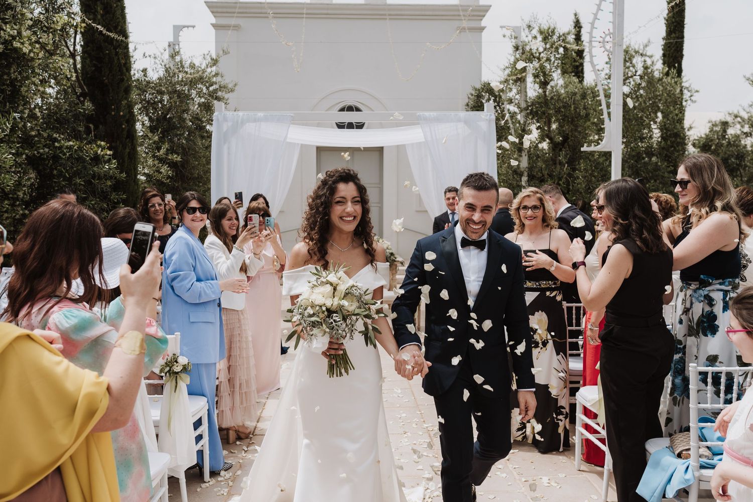 Guests shower confetti on newlyweds walking down the aisle at an outdoor wedding ceremony.
