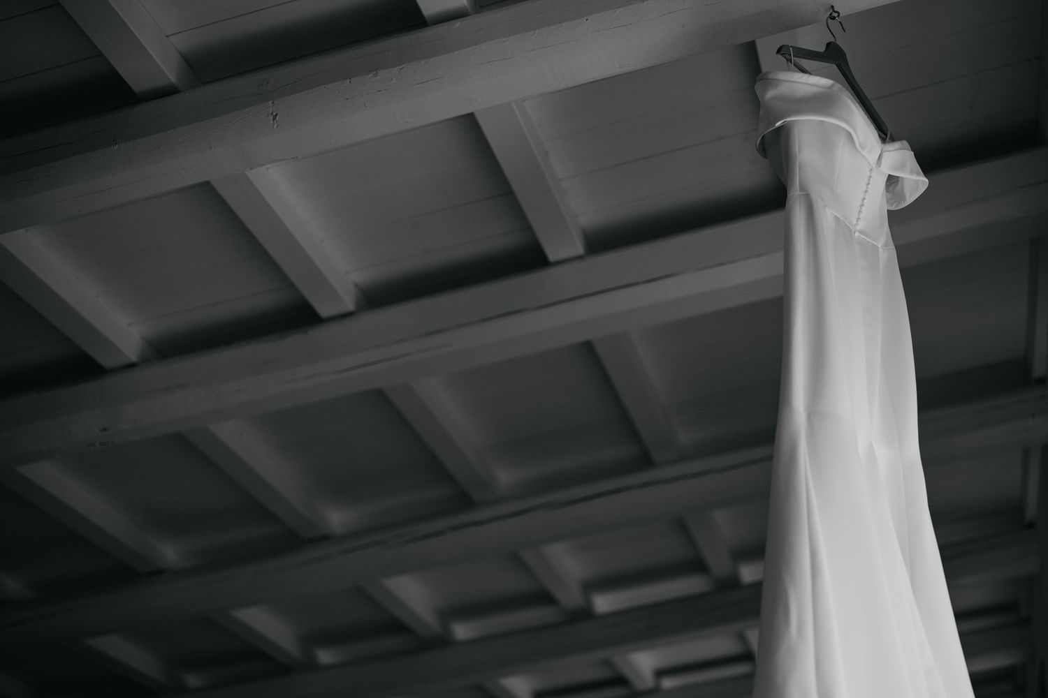 A white fabric or dress hangs elegantly from wooden ceiling beams.
