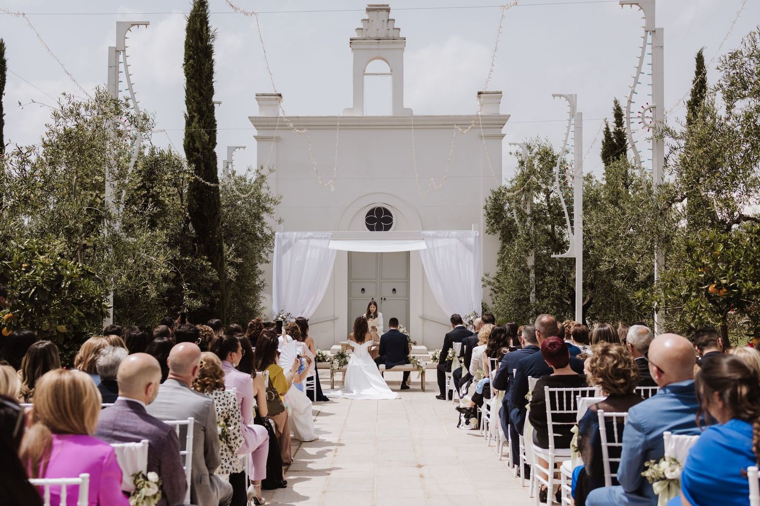 White chapel wedding ceremony setup with rows of chairs and cypress trees lining the aisle.