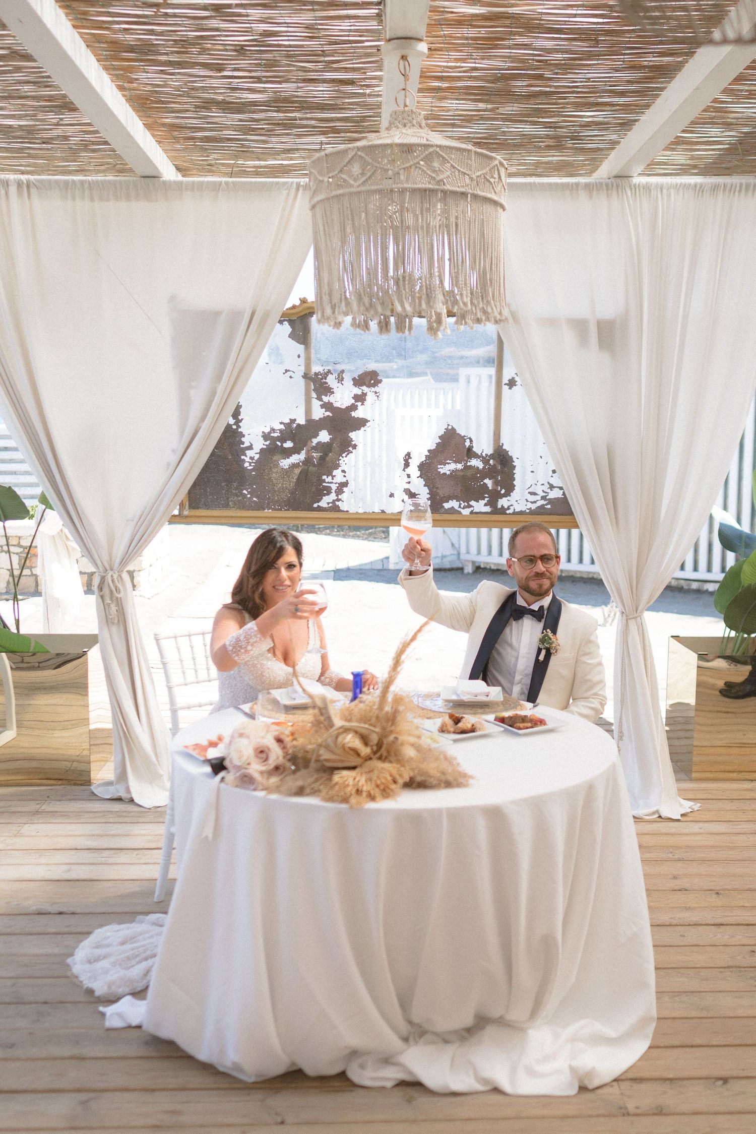 Elegant beach wedding reception setup with white drapes and tablecloths in an oceanfront pavilion.