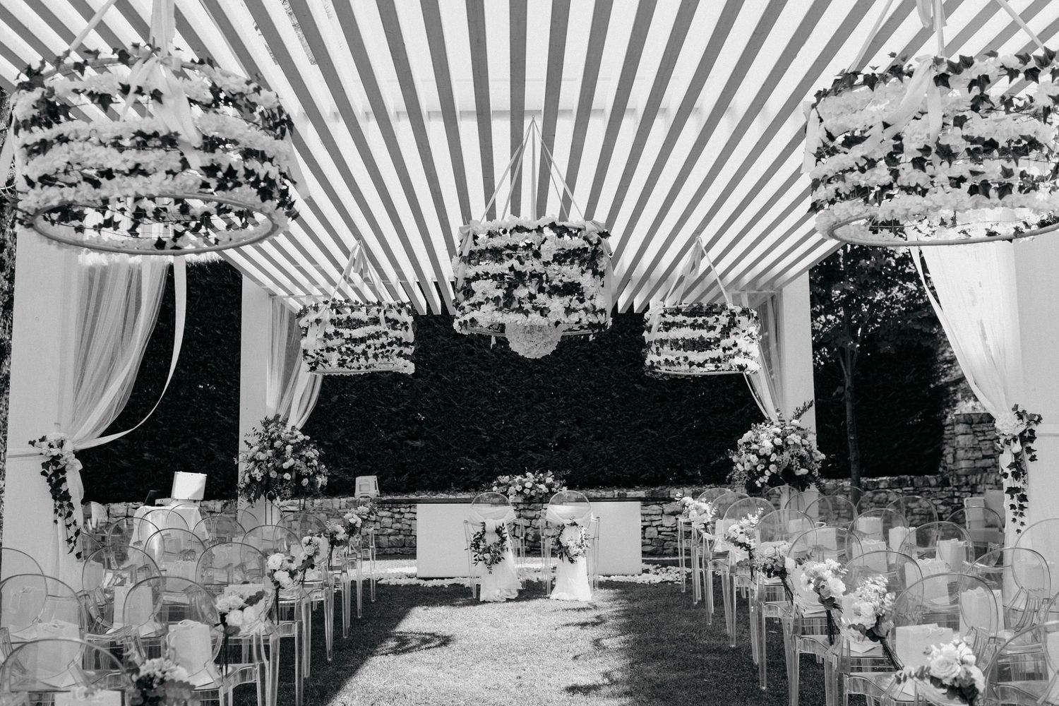 Elegant black and white wedding ceremony setup with draped ceiling, floral chandeliers and rows of white chairs.