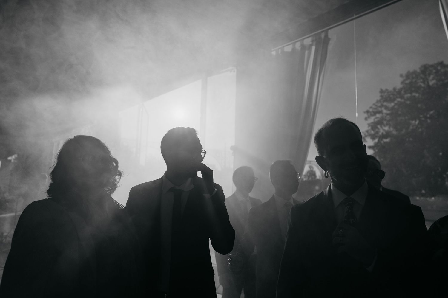 Dramatic black and white silhouette of wedding guests in smoke-filled reception venue.