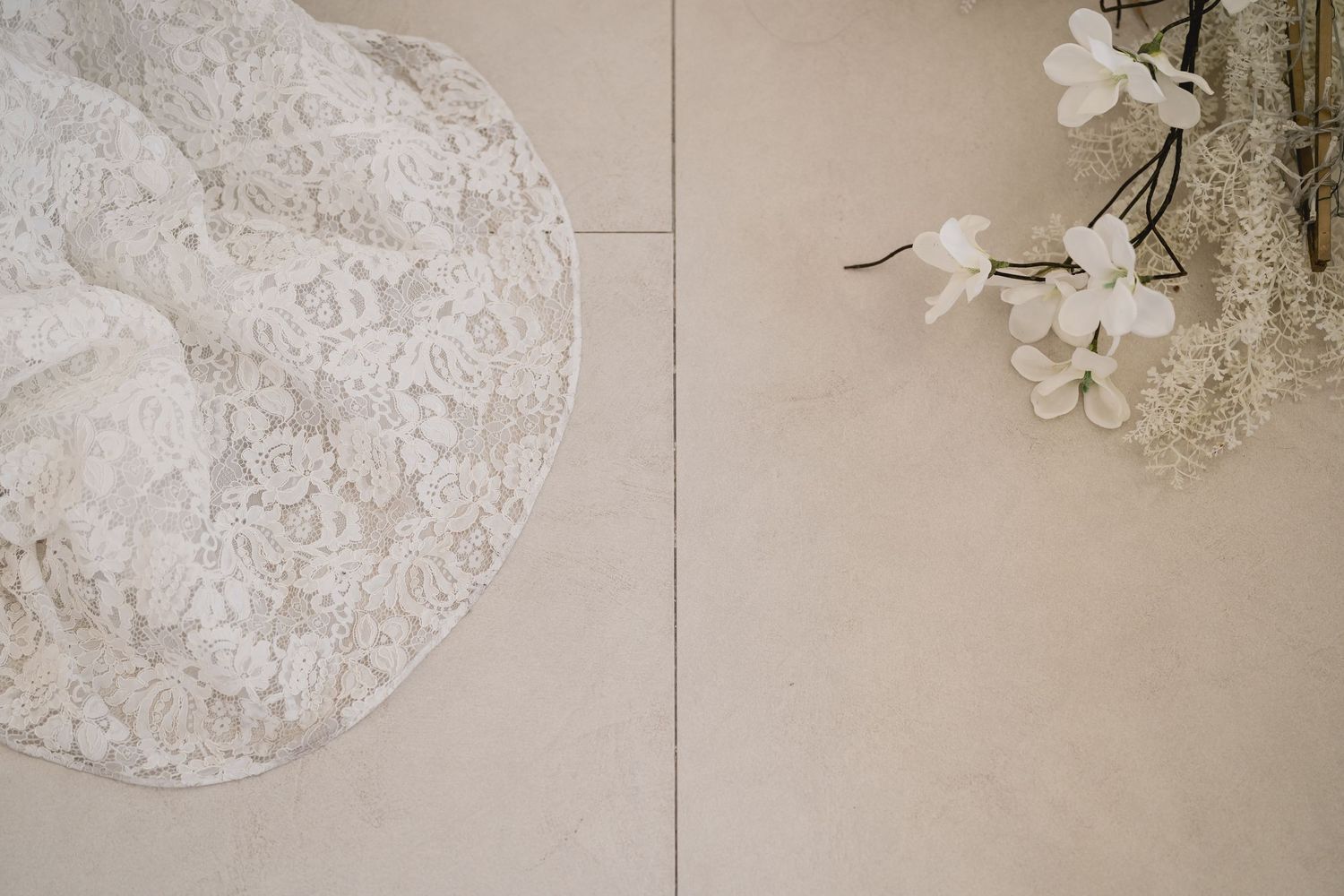 Detail shot of white lace wedding dress fabric next to delicate floral decorations.