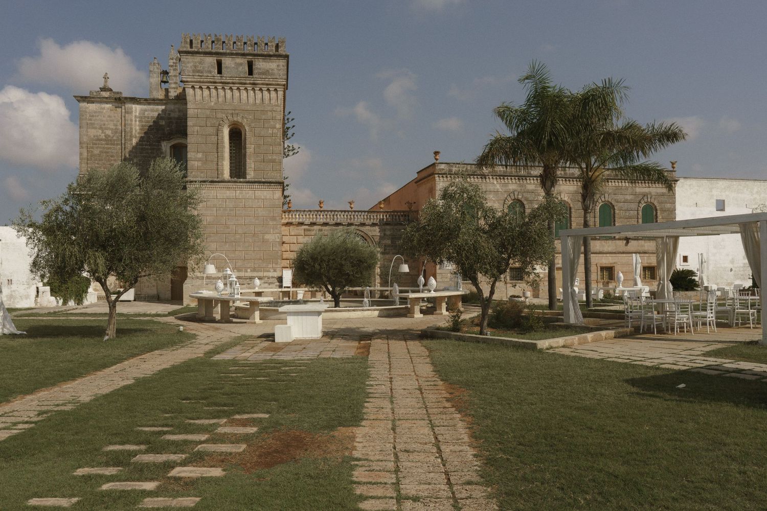 Stone tower and walkway in historic church complex with palm trees and white buildings under blue sky in Florida.
