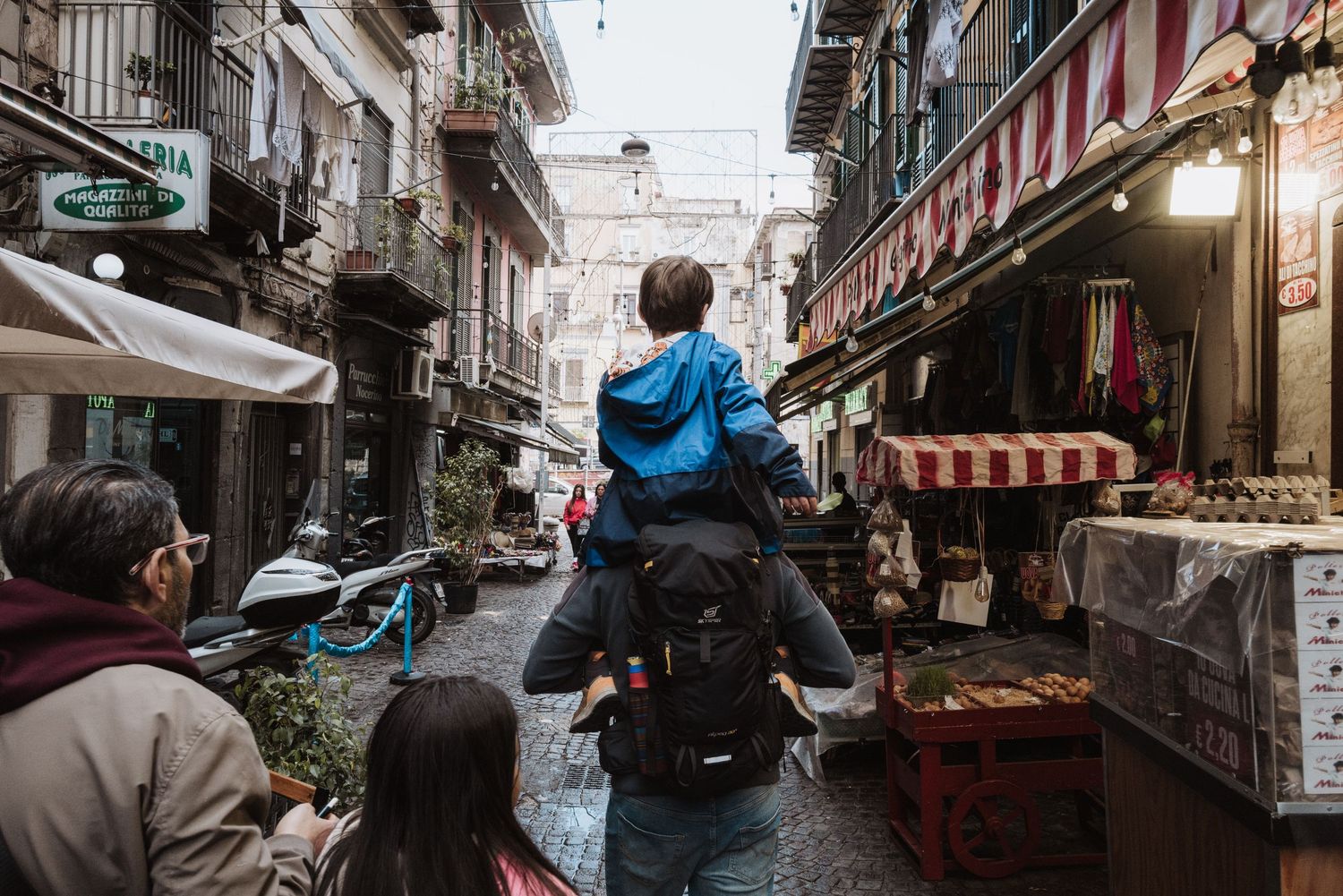 Narrow alley in an urban market district with shops and pedestrians.