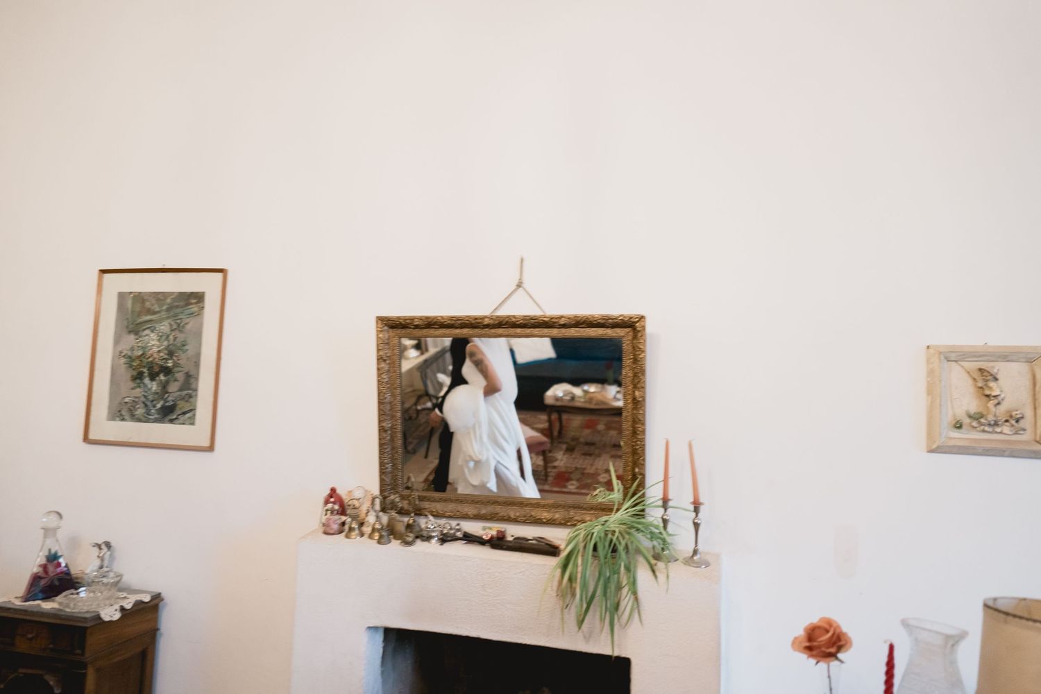 A mirror decorated with greenery and candles sits above a white fireplace mantel.
