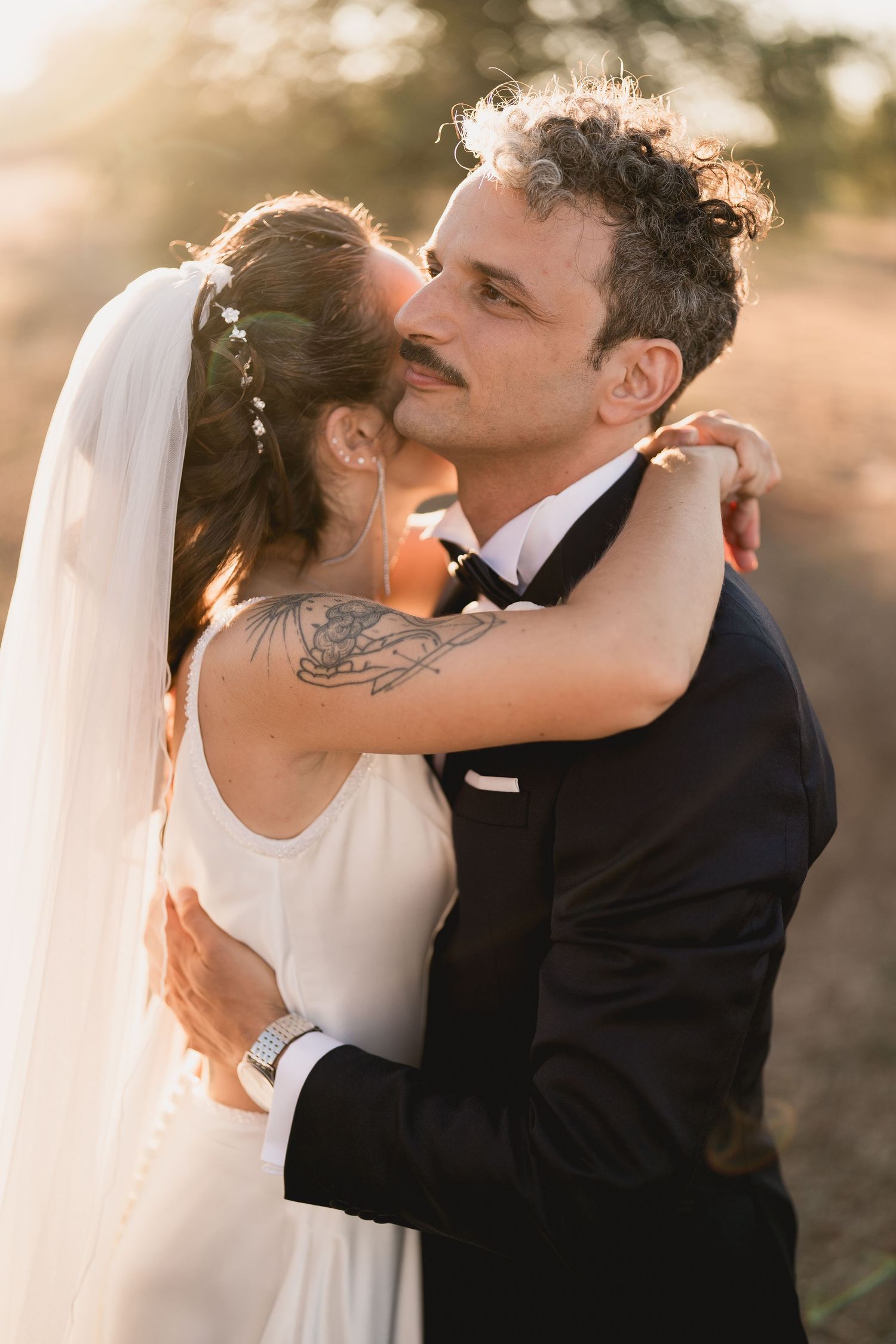 A tender wedding moment captured at golden hour as newlyweds embrace, with the bride in a flowing white dress and veil.