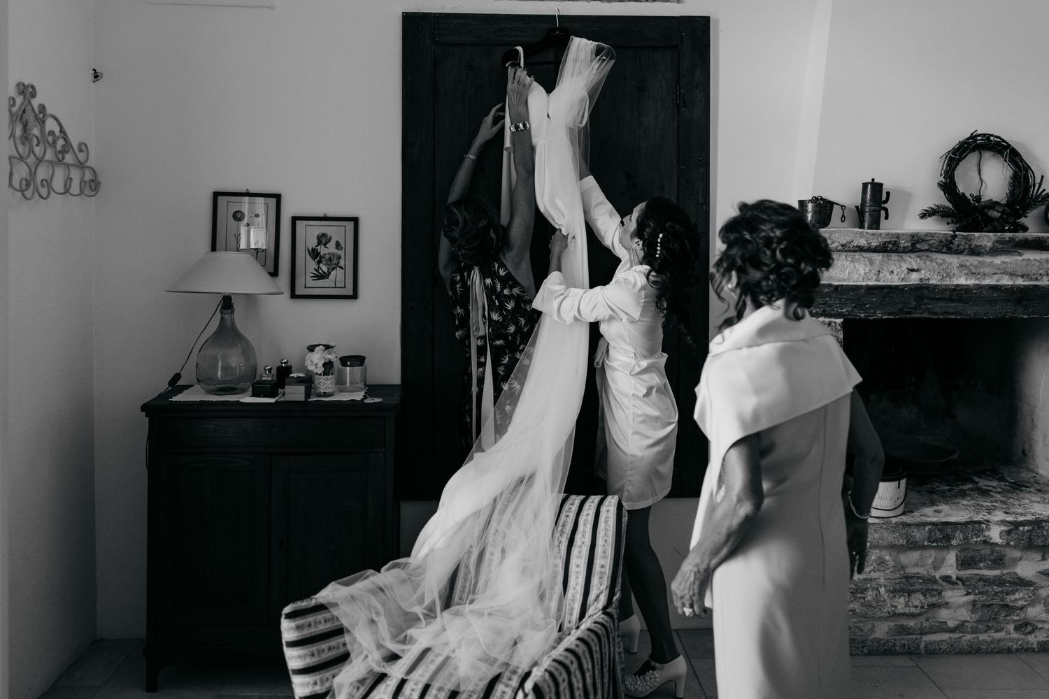 A black and white photo showing wedding dress preparations in a vintage-style room.