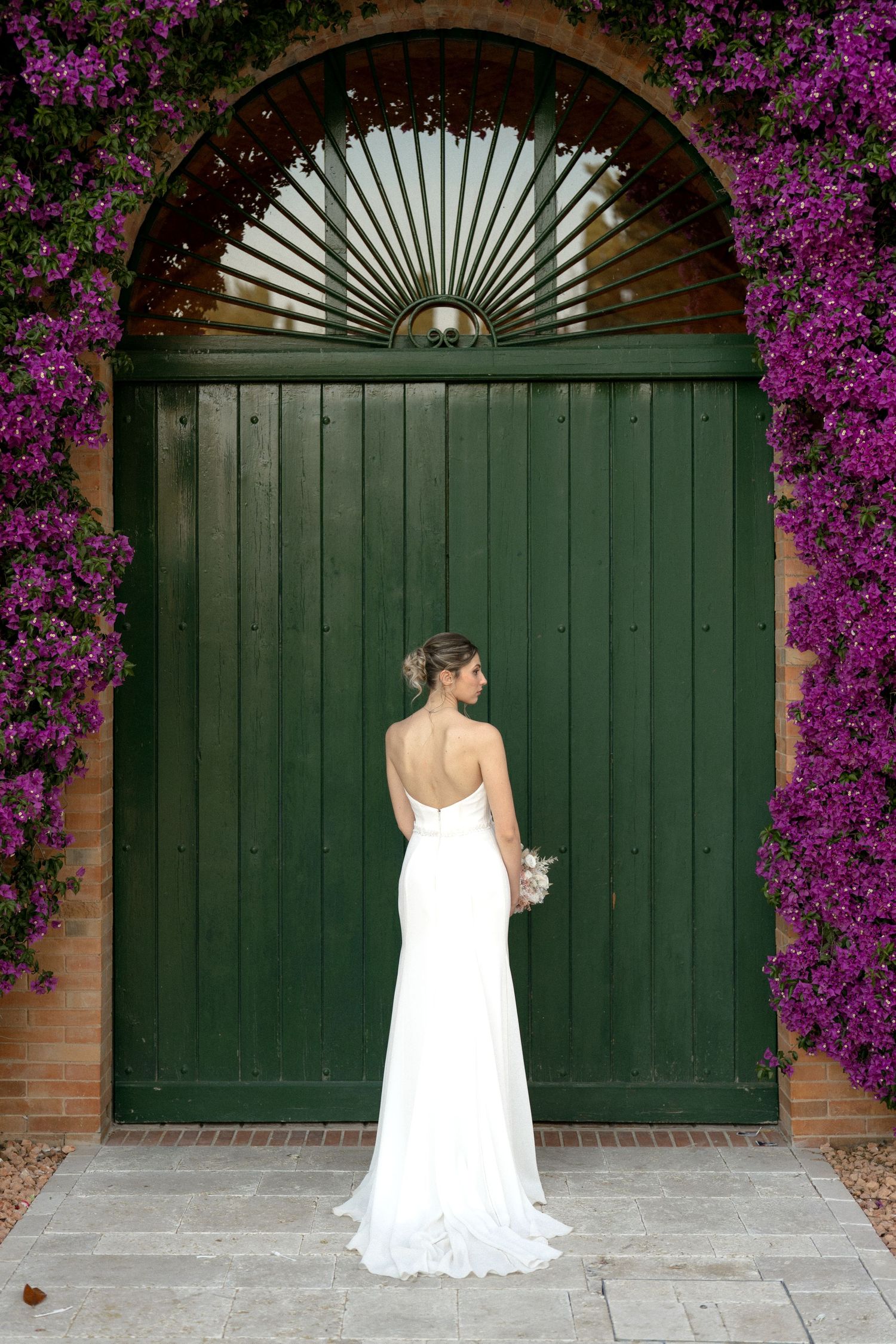 Bridal portraits against green wooden doors framed by vibrant purple flowers.