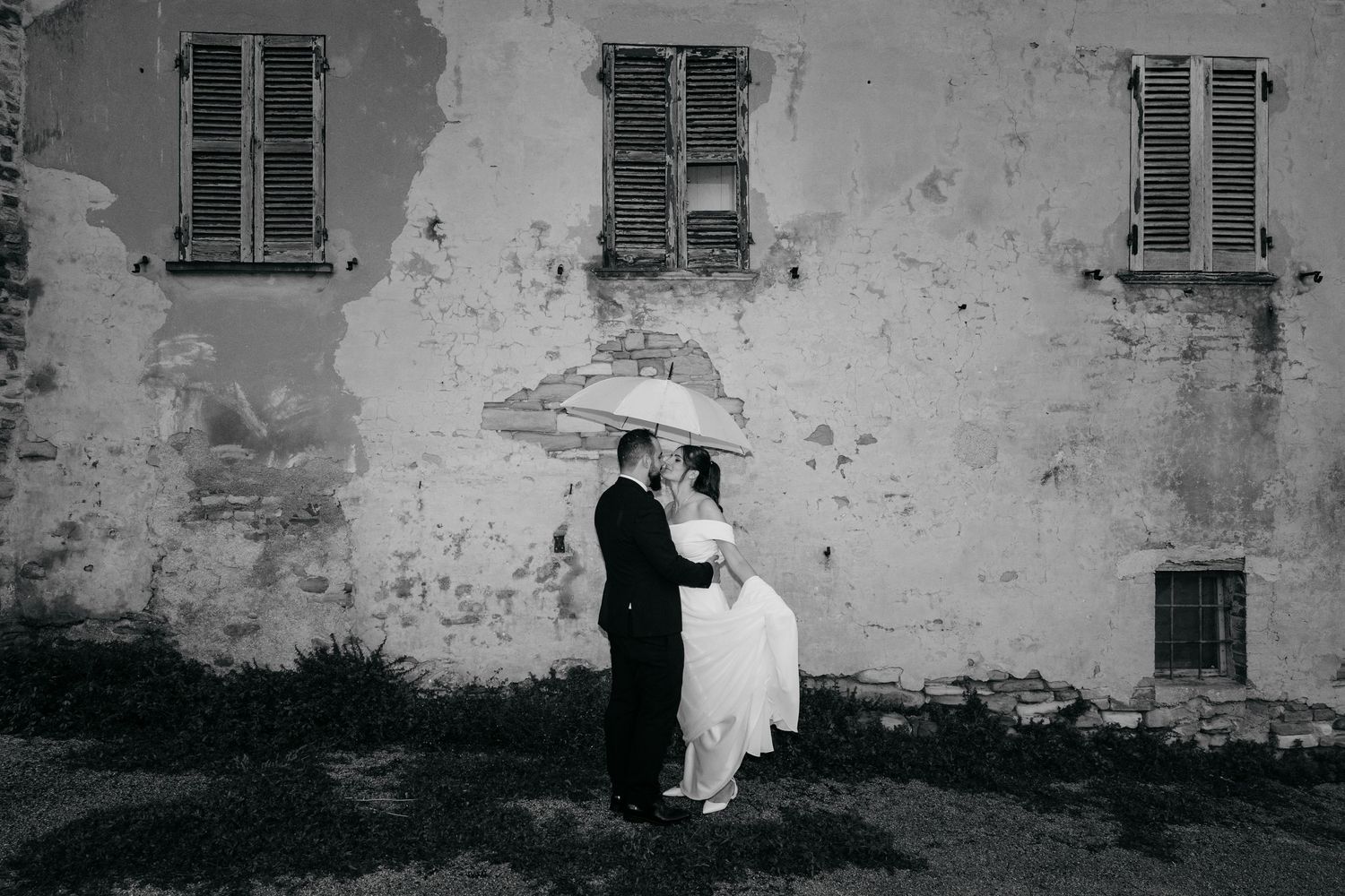 Wedding couple silhouettes against a weathered stone wall in black and white photography.