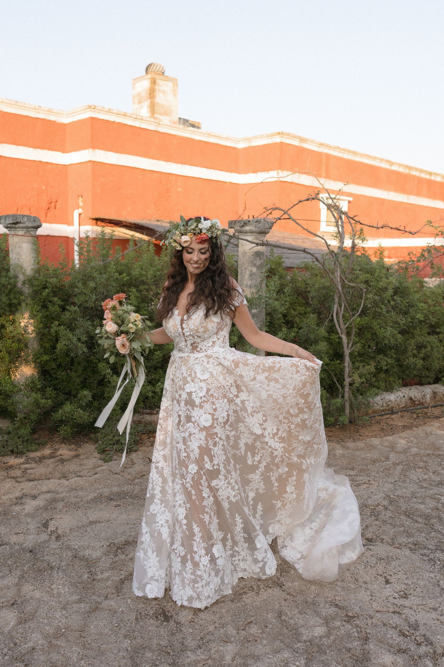 Bride twirling in a lace wedding dress against an orange wall and garden backdrop.