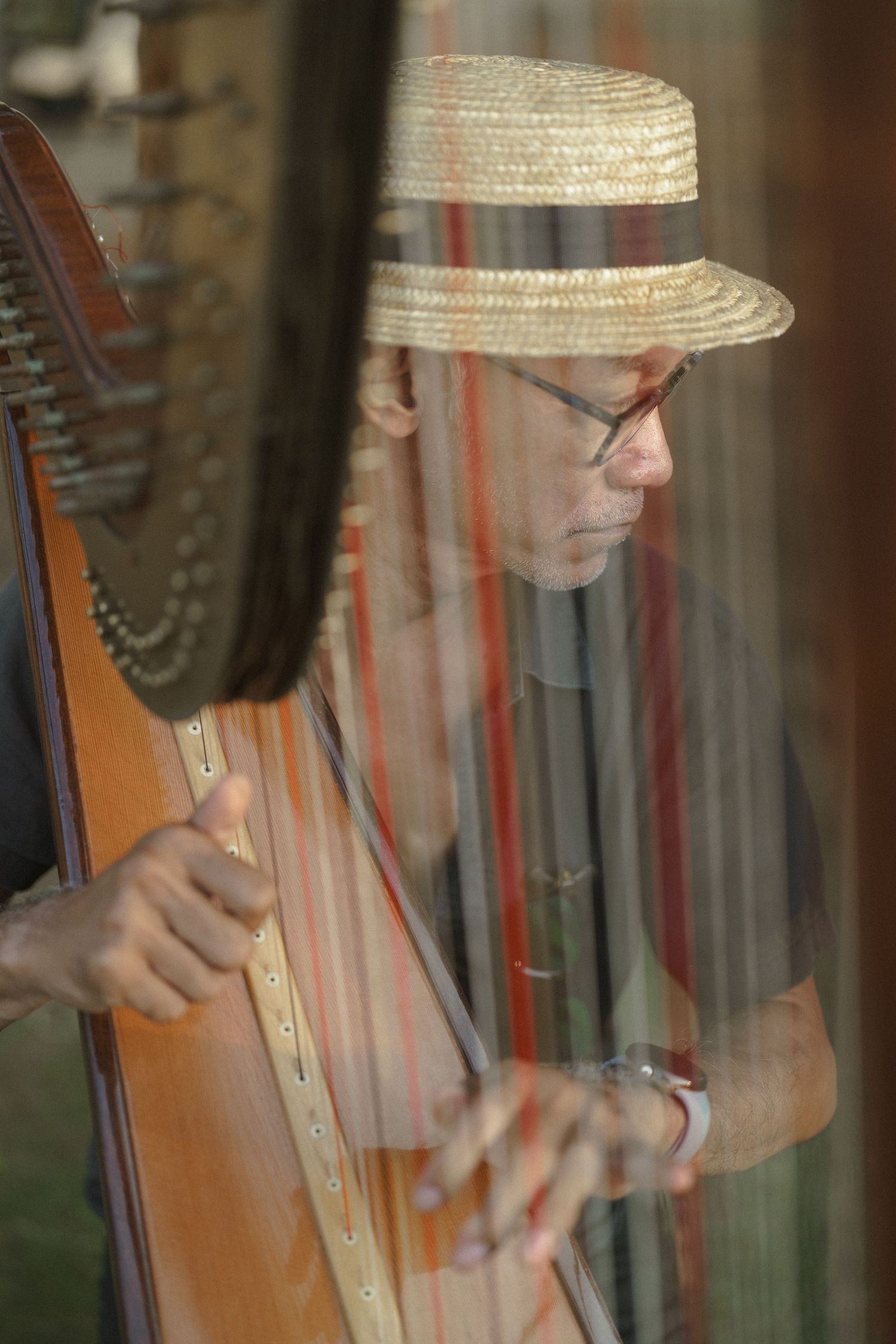 A musician wearing a straw boater hat plays a large concert harp indoors.