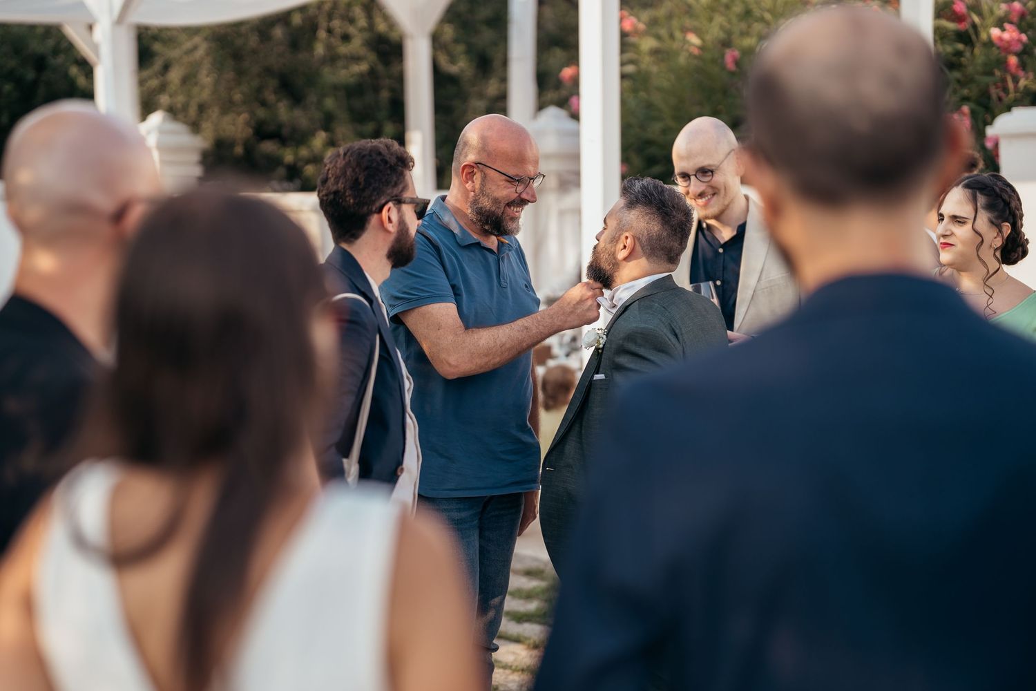 Casual outdoor wedding reception gathering under a white gazebo on a sunny day.