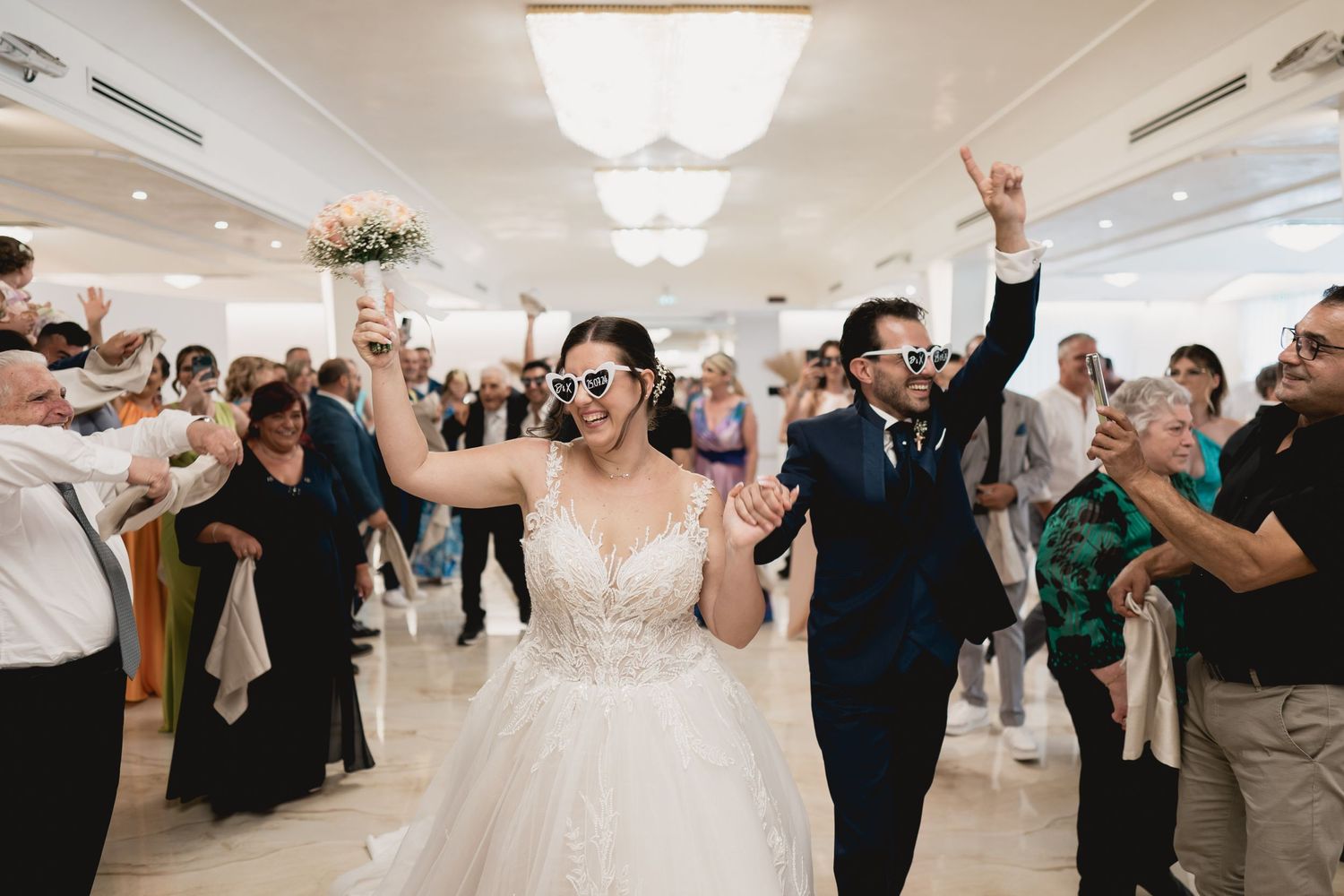 Wedding celebration with guests dancing and cheering in a bright reception hall.
