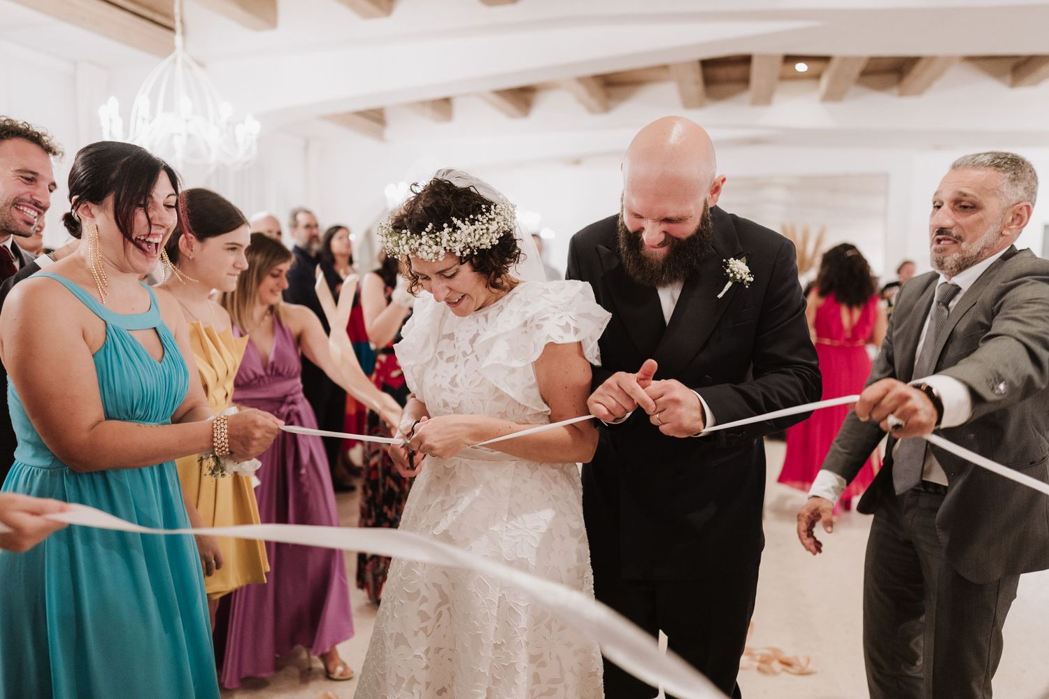 Wedding ceremony moment with guests in colorful attire participating in a ribbon cutting tradition.