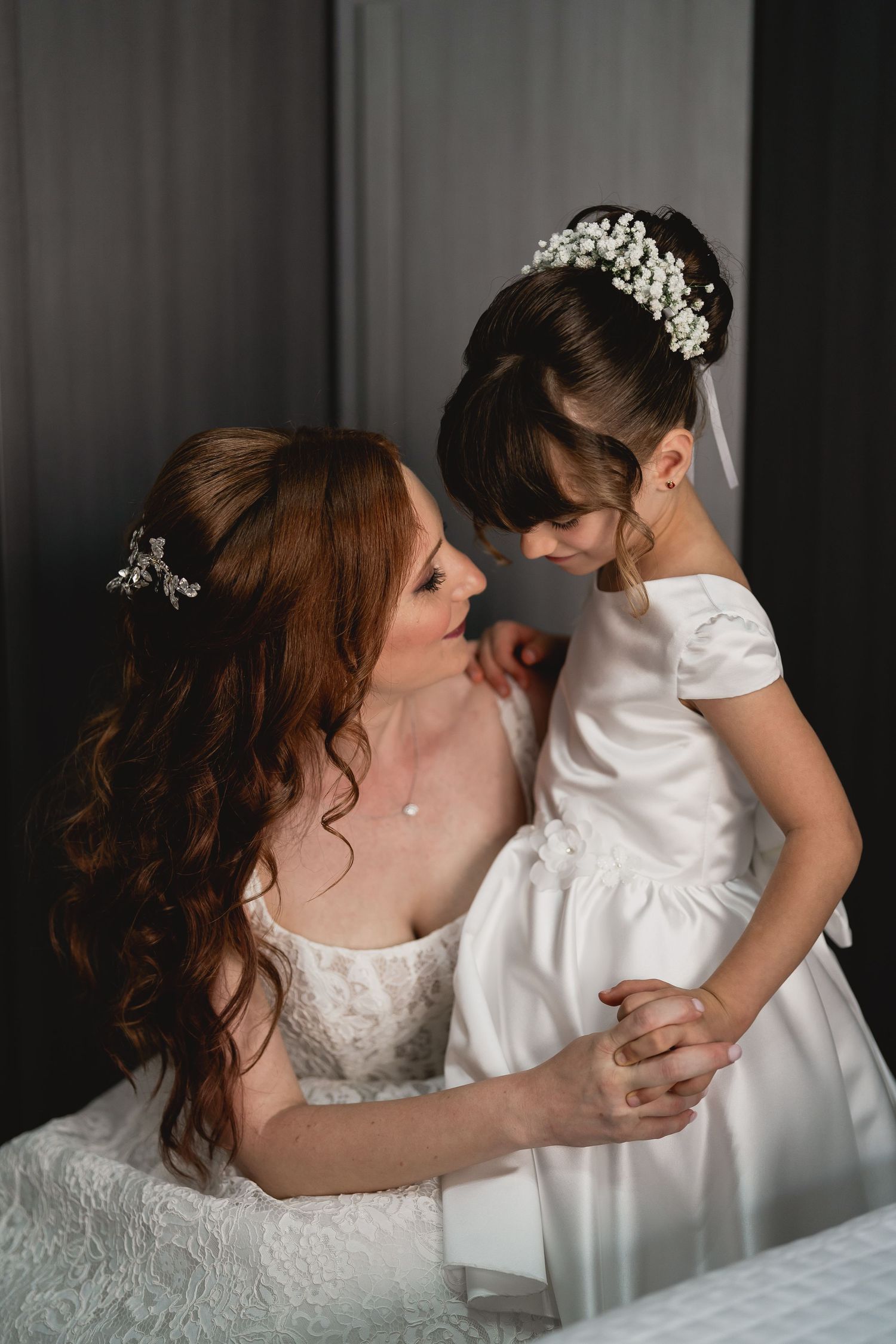 Tender moment between two figures in matching white formal dresses with ornate hair accessories.