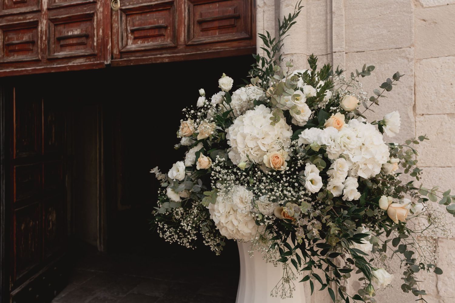 Elegant white floral arrangement with eucalyptus leaves decorates a wooden church entrance.