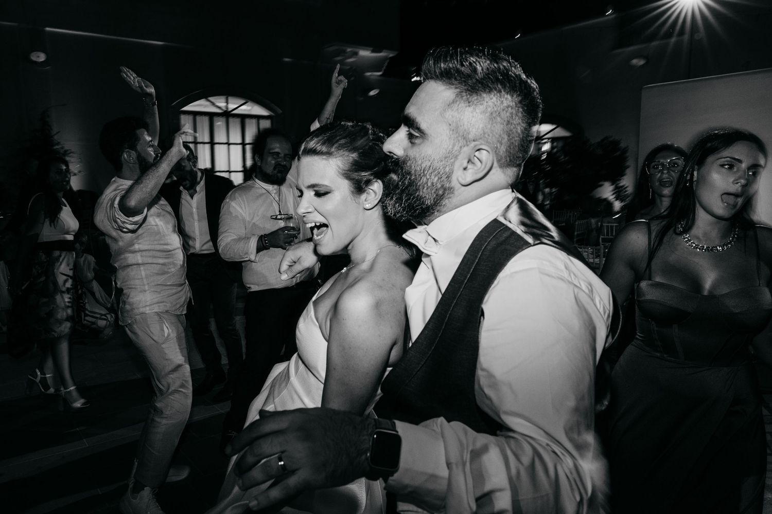 Black and white photo captures dancing party guests in formal attire at a nightclub venue.