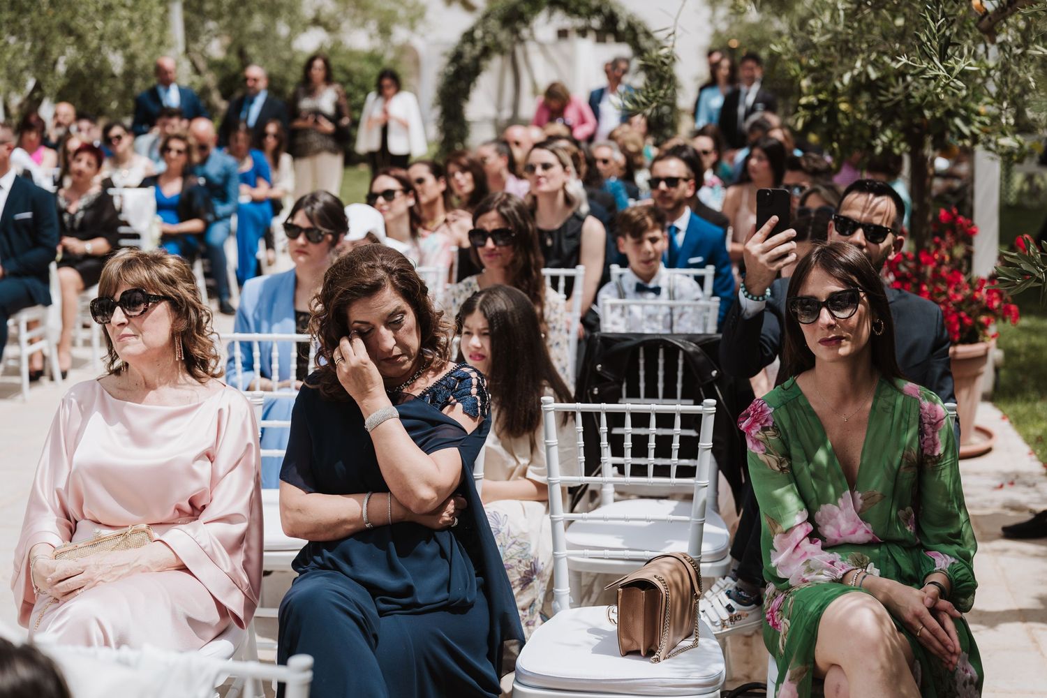 Wedding guests seated in white chairs at outdoor ceremony venue.