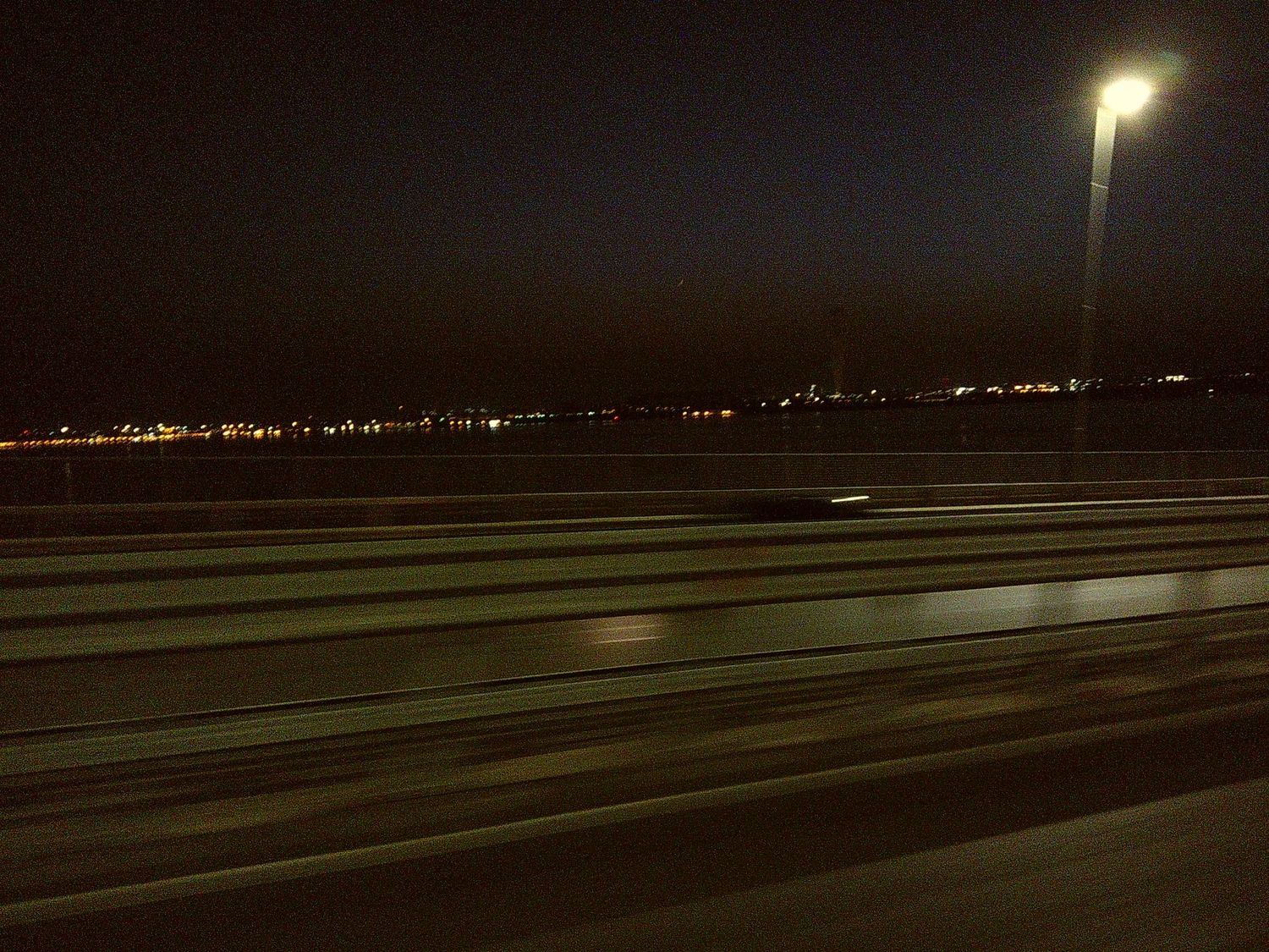 Night view of empty highway lanes with city lights glowing in the distance.